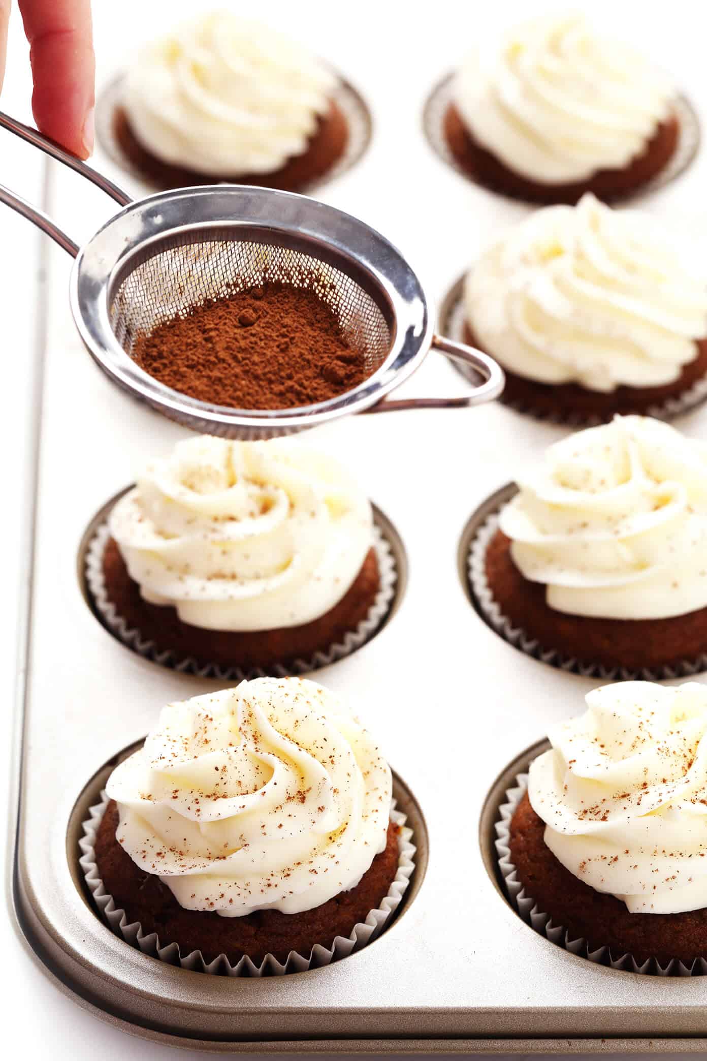 These pumpkin cupcakes are quick and easy to make, perfectly moist and fluffy and flavorful, and topped with the most heavenly cream cheese frosting. | gimmesomeoven.com #pumpkin #cupcakes #cake #creamcheese #frosting #icing #thanksgiving #halloween #fall #dessert Sprinkling Cinnamon on Pumpkin Cupcakes
