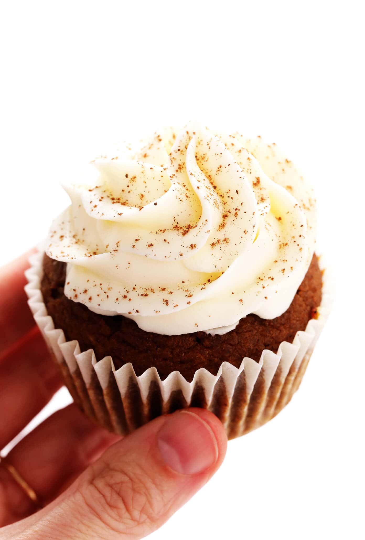 These pumpkin cupcakes are quick and easy to make, perfectly moist and fluffy and flavorful, and topped with the most heavenly cream cheese frosting. | gimmesomeoven.com #pumpkin #cupcakes #cake #creamcheese #frosting #icing #thanksgiving #halloween #fall #dessert Holding a Pumpkin Cupcake with Cream Cheese Frosting