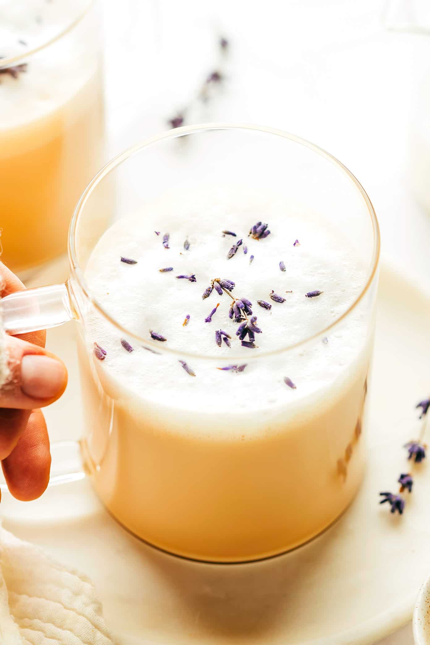 This cozy London Fog (Earl Grey) latte recipe is easy to make hot or iced and brewed with a lovely hint of lavender, vanilla, honey and your choice of milk. It's the perfect cozy drink to warm you up in the winter or a refreshing drink to cool off in the summer, and always so delicious! | gimmesomeoven.com Holding a mug of London Fog Latte