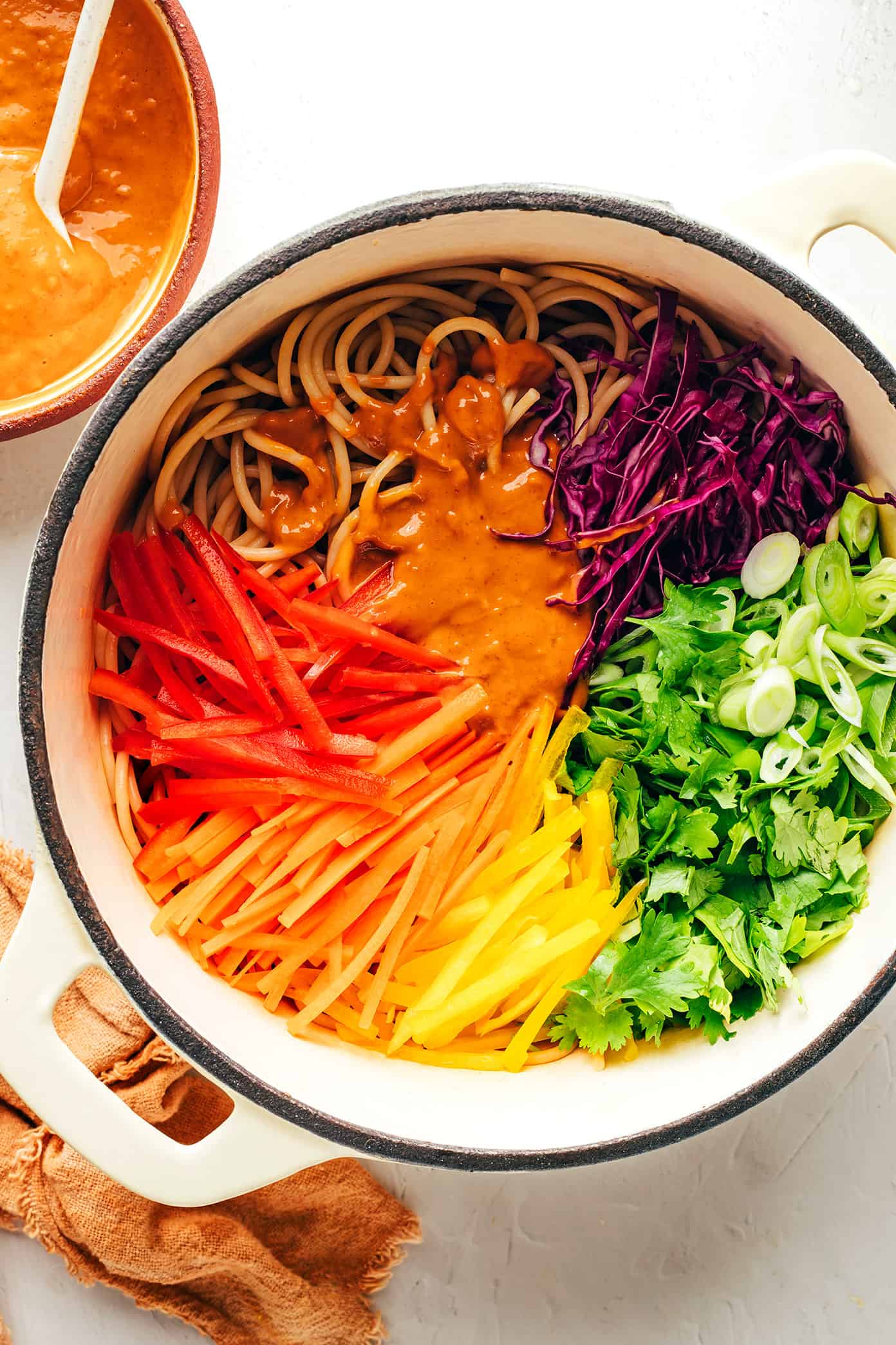 This rainbow peanut noodles recipe is made with colorful fresh veggies, your choice of noodles, and the most irresistible sesame-lime peanut sauce. Feel free to add in a protein (chicken, shrimp, beef, tofu, etc), serve warm or cold, and use whatever colorful vegetables you have on hand. Perfect for easy meal prep too! | gimmesomeoven.com Mixing together rainbow peanut noodles