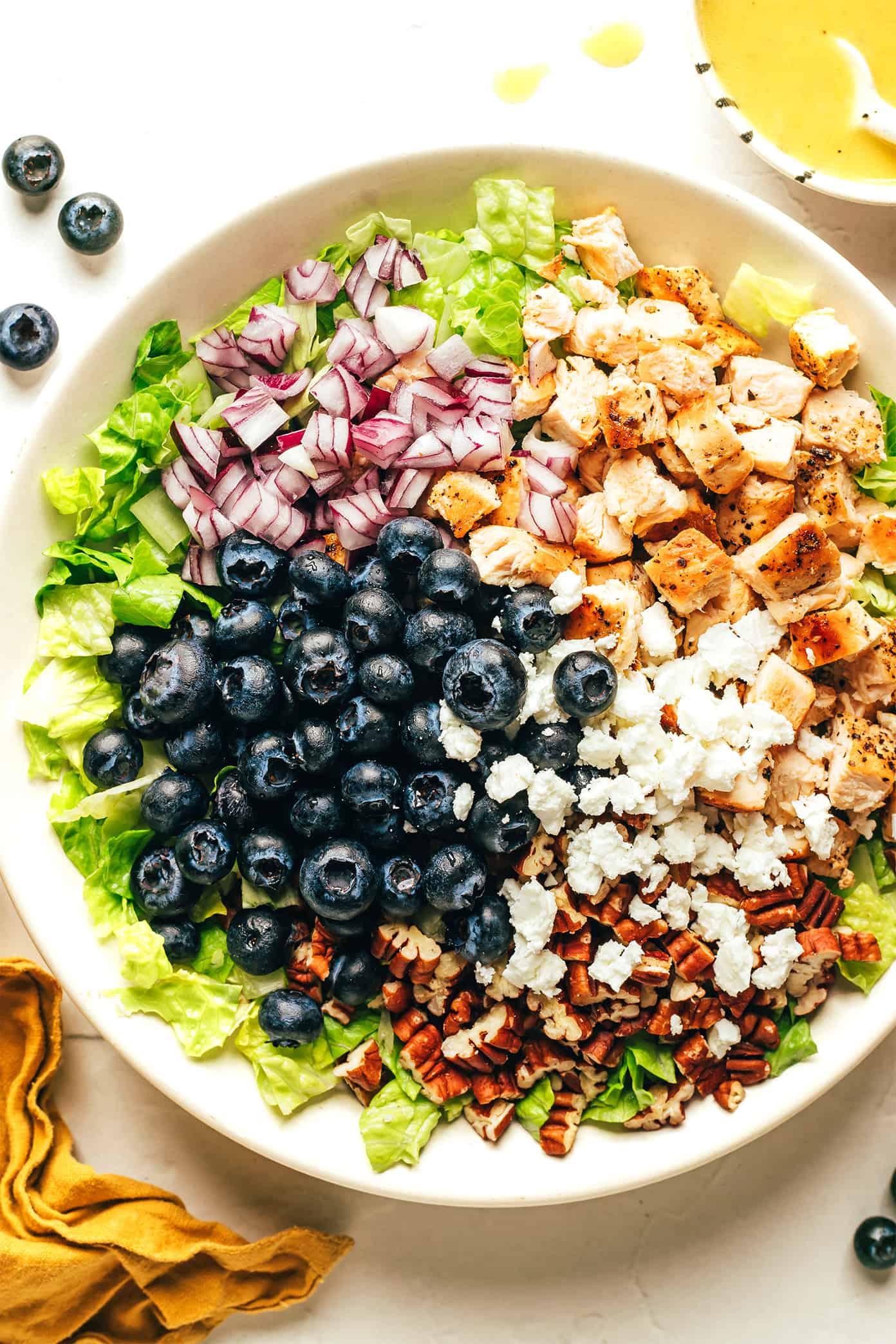 This blueberry chicken chopped salad recipe is loaded up with your choice of greens, tangy feta or goat cheese, diced red onion, toasted pecans, and tossed with a simple lemon vinaigrette. Feel free to swap steak, shrimp, salmon or roasted chickpeas as the protein. Always a delicious and healthy dinner! | gimmesomeoven.com Blueberry Chicken Chopped Salad Ingredient in Bowl