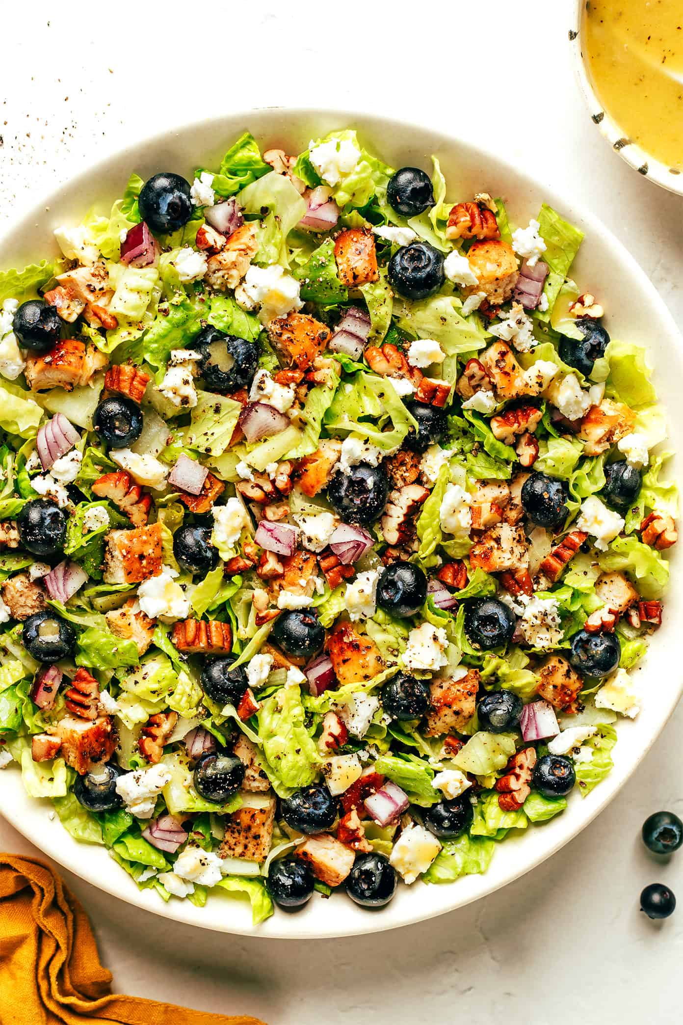 This blueberry chicken chopped salad recipe is loaded up with your choice of greens, tangy feta or goat cheese, diced red onion, toasted pecans, and tossed with a simple lemon vinaigrette. Feel free to swap steak, shrimp, salmon or roasted chickpeas as the protein. Always a delicious and healthy dinner! | gimmesomeoven.com Blueberry Chicken Chopped Salad in Bowl with Lemon Vinaigrette