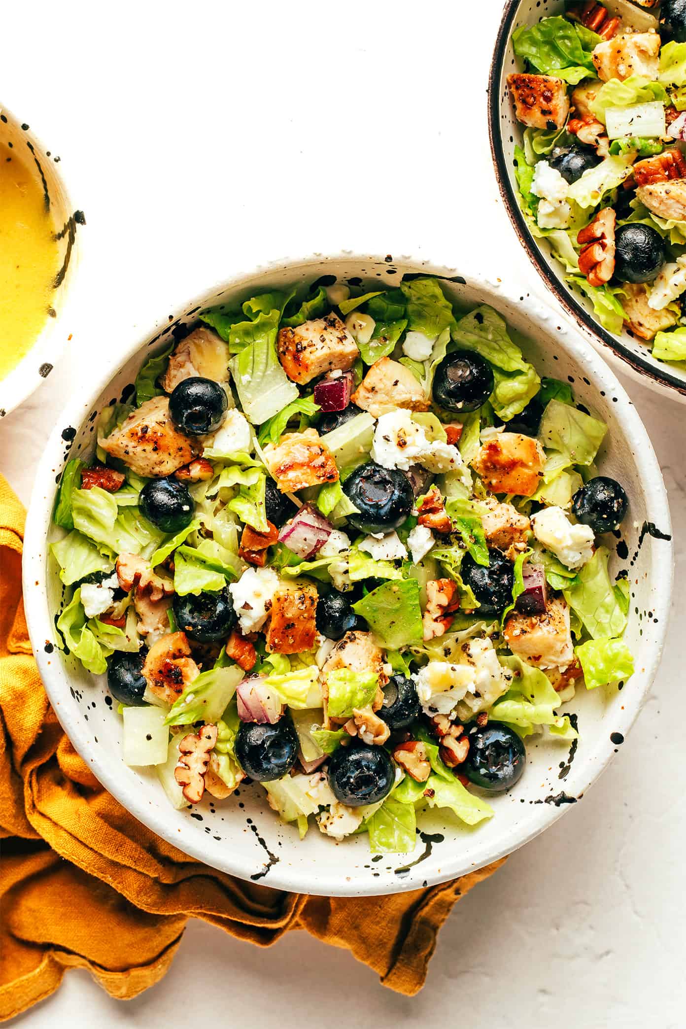 This blueberry chicken chopped salad recipe is loaded up with your choice of greens, tangy feta or goat cheese, diced red onion, toasted pecans, and tossed with a simple lemon vinaigrette. Feel free to swap steak, shrimp, salmon or roasted chickpeas as the protein. Always a delicious and healthy dinner! | gimmesomeoven.com Blueberry salad in small bowls