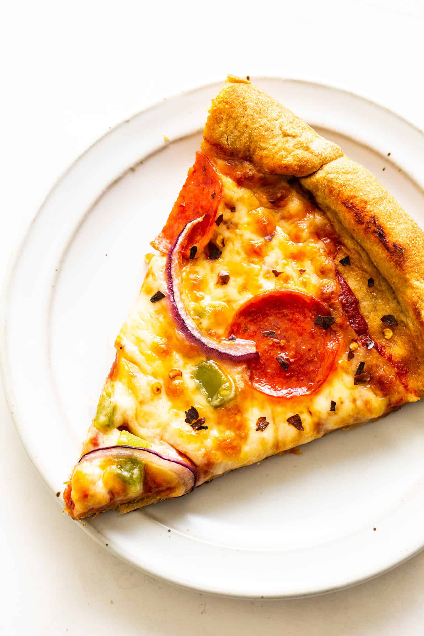 My favorite homemade whole wheat pizza dough recipe is easy to make by hand or with a stand mixer, it's naturally sweetened with a hint of honey, and it's always perfectly chewy and delicious. Feel free to add Italian seasoning, garlic, or Parmesan to your pizza crust too if you'd like! | gimmesomeoven.com Slice of homemade pizza with whole wheat dough on plate