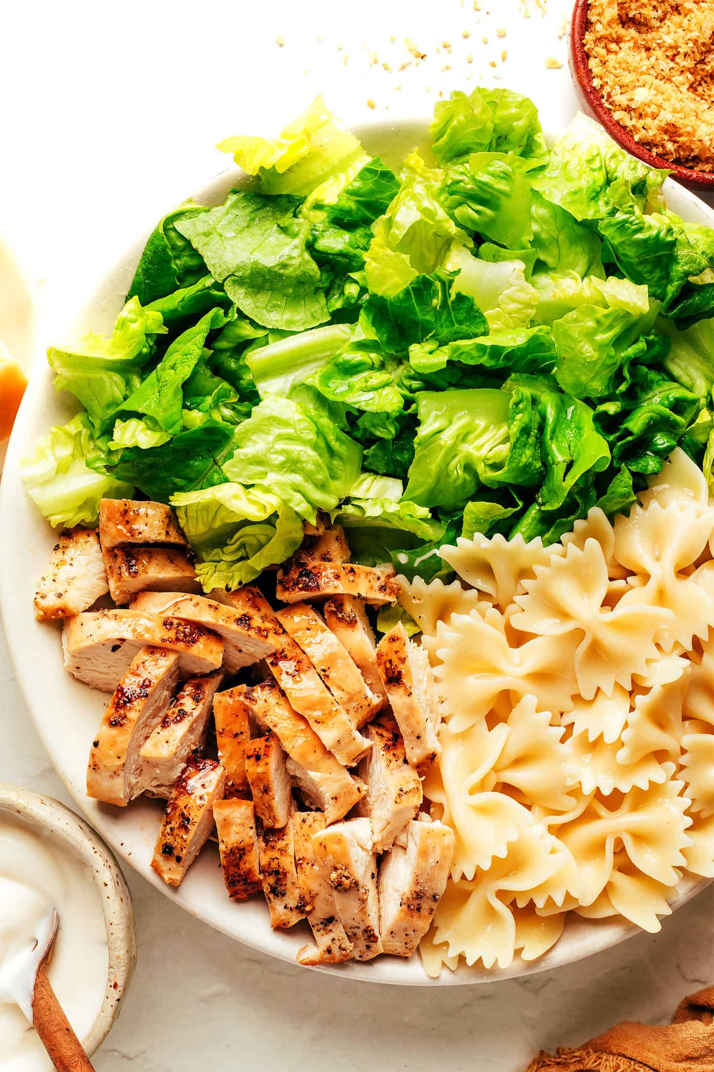 This Chicken Caesar Pasta Salad recipe is tossed with my favorite Caesar dressing, lots of Parmesan cheese, and the yummiest garlicky breadcrumbs. Feel free to use a different protein (such as salmon, shrimp, Italian sausage, bacon or roasted chickpeas) for the chicken if you prefer! | gimmesomeoven.com Chicken caesar pasta salad ingredients in bowl