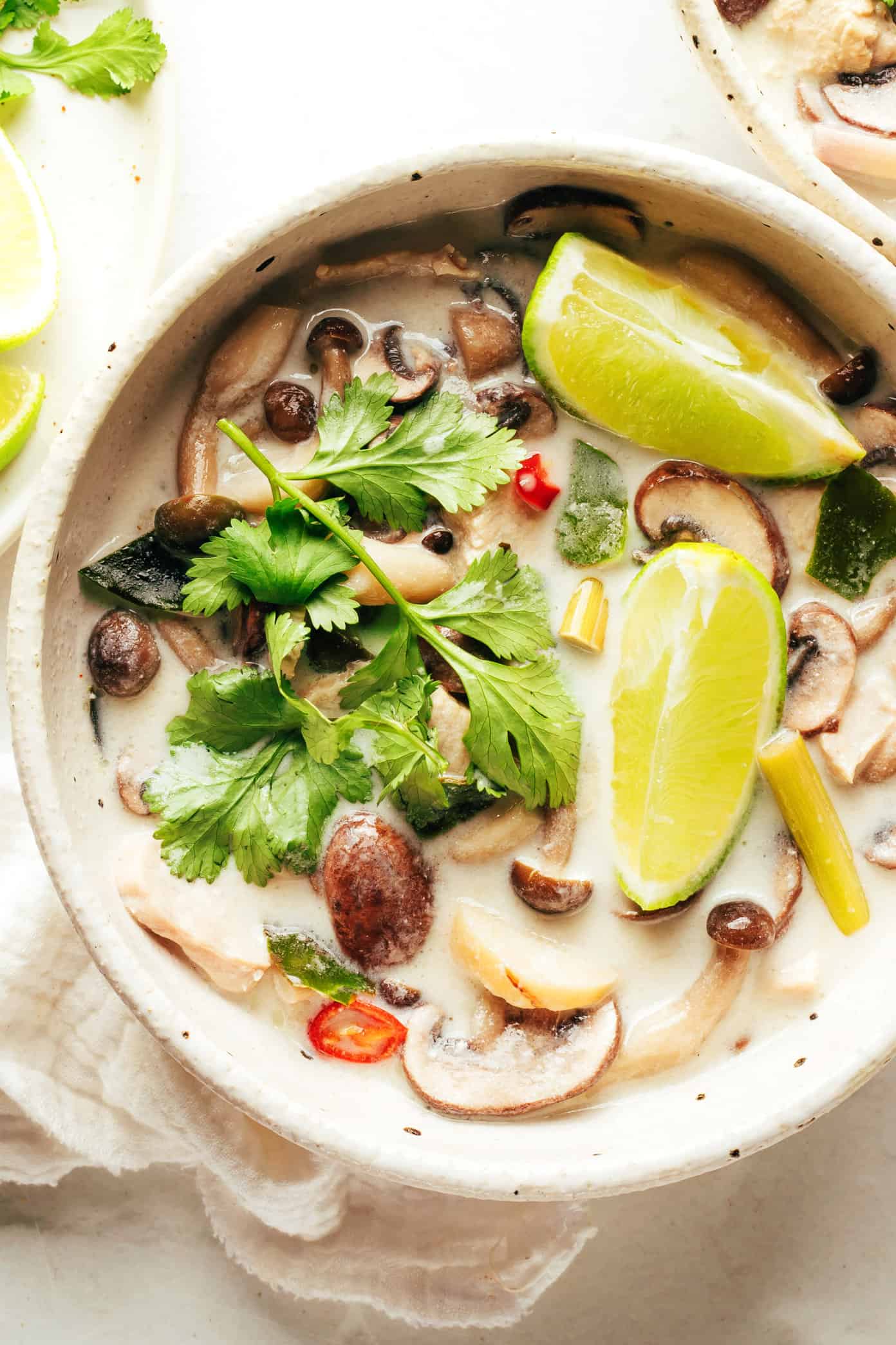 tom kha gai in a bowl with limes and cilantro