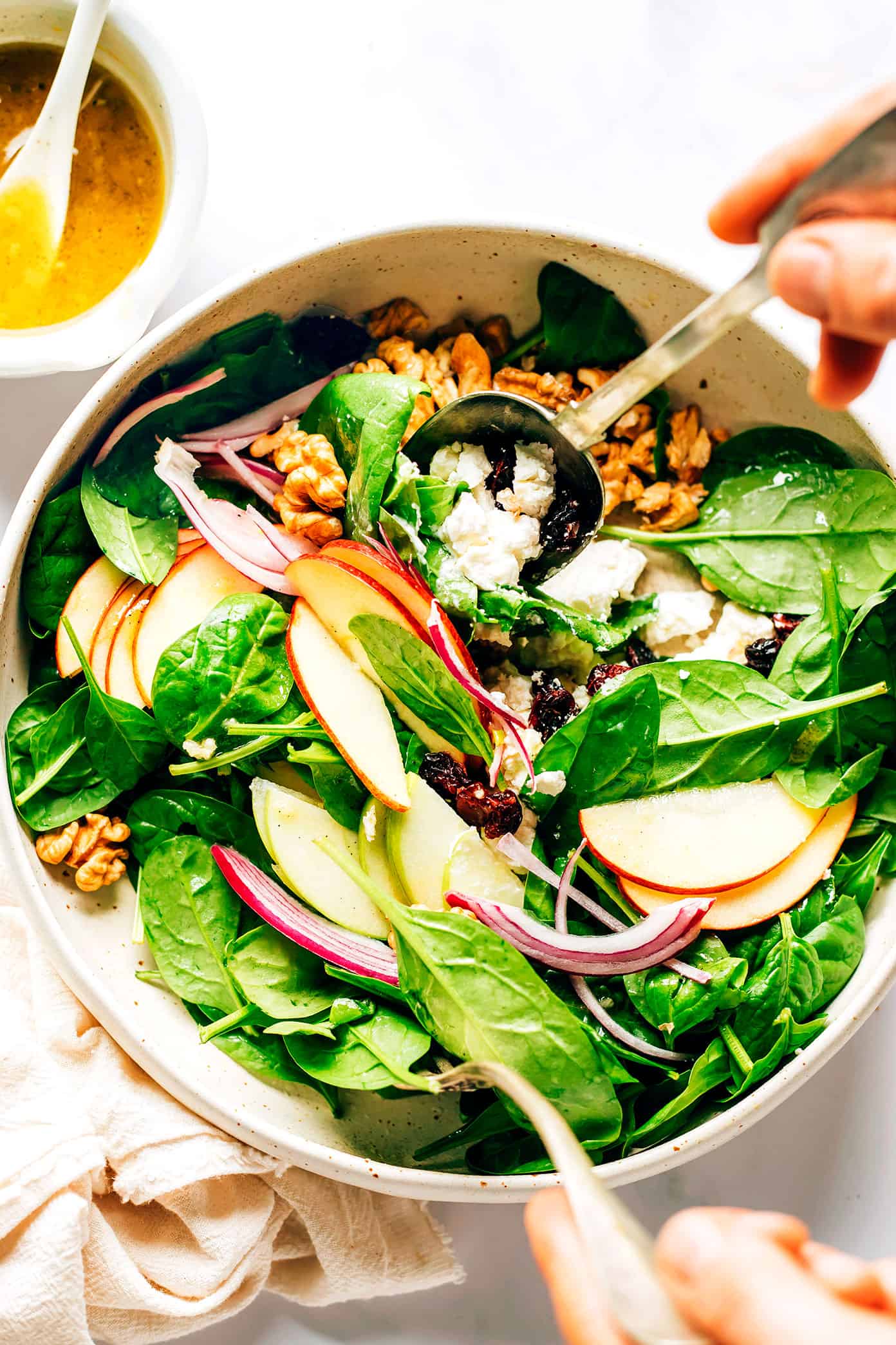 This classic apple spinach salad is tossed with your choice of nuts (walnuts, pecans, or almonds), cheese (blue, feta, goat, or cheddar), dried cranberries, red onions, and a simple vinaigrette. It's the perfect side salad on its own, or feel free to add some protein or avocado to make it an entree! | gimmesomeoven.com Tossing Apple Spinach Salad in a mixing bowl