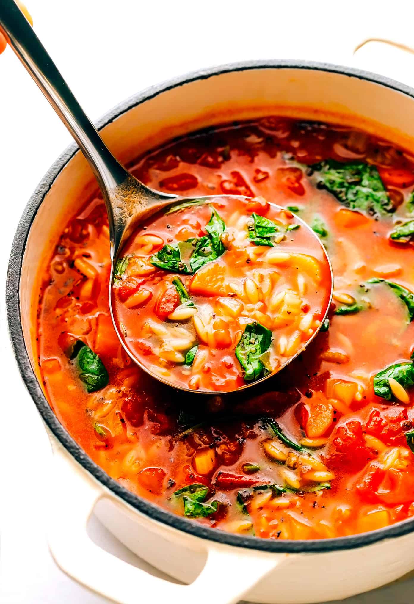 This Italian Orzo Spinach Soup is simmered with hearty pasta, veggies, greens in a zesty tomato-herb broth, then served warm with lots of Parmesan and fresh basil. It's one of our favorite vegetarian 30 minute meals, but feel free to add in sausage or chicken too if you'd like! | gimmesomeoven.com Italian Orzo Soup in pot with ladle