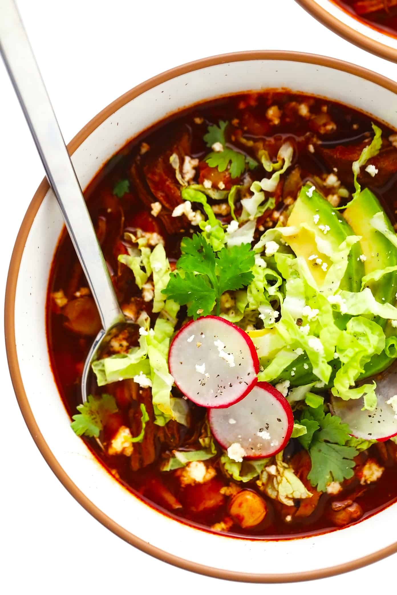 This traditional Mexican pozole recipe is made with tender pork and hominy and simmered in the most delicious chile broth, then piled high with your favorite fresh toppings. Crock-Pot and Instant Pot options for this soup are included too! | gimmesomeoven.com Bowl of pork pozole with avocado, radishes, cilantro and cabbage