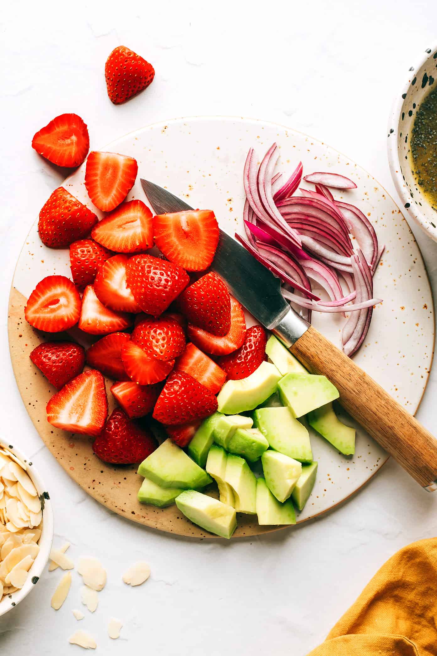 This fresh strawberry spinach salad recipe is tossed with creamy avocado, toasted almonds, sliced red onion, your choice of cheese (blue, feta, goat) and a lightly-sweetened honey poppyseed dressing. Feel free to add in some grilled chicken, shrimp or bacon if you'd like too! | gimmesomeoven.com Slicing strawberries, avocado and red onion