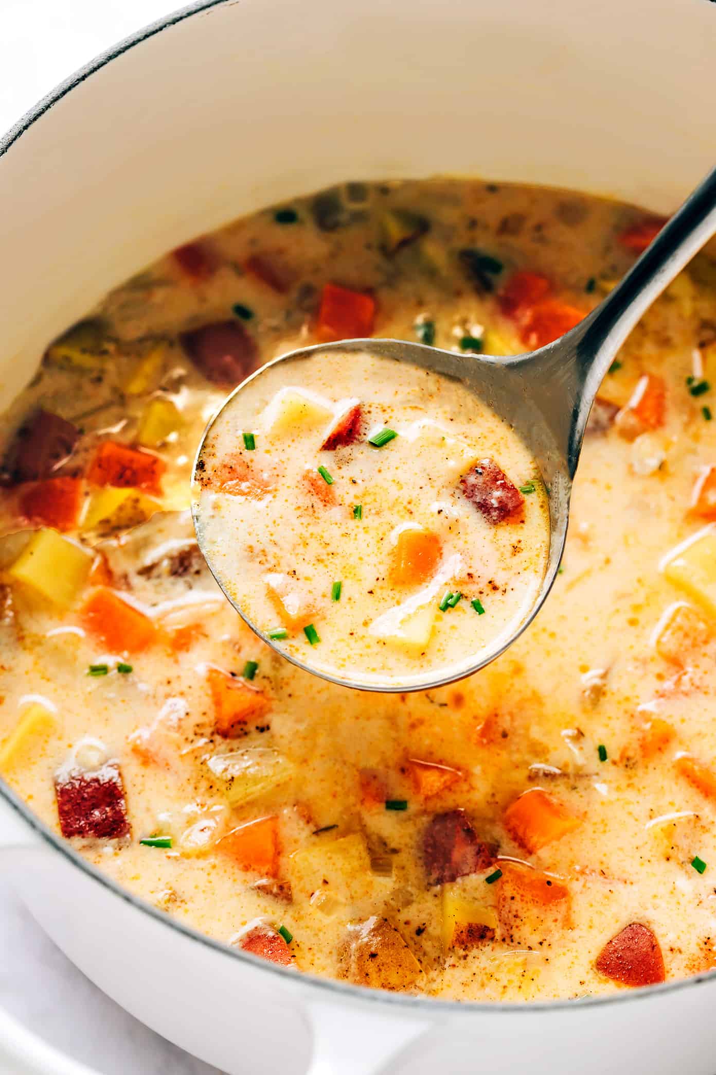 This Three Potato Soup is made with a zesty, creamy cheddar broth and a sweet and savory combination of Yukon gold potatoes, red potatoes, and sweet potatoes. Easy to make in about 30 minutes and always so delicious and comforting! Feel free to leave the soup vegetarian, or add in some bacon, ham, sausage or chicken if you prefer. (Gluten-free and vegan options included too.) | gimmesomeoven.com Pot full of three potato soup with ladle
