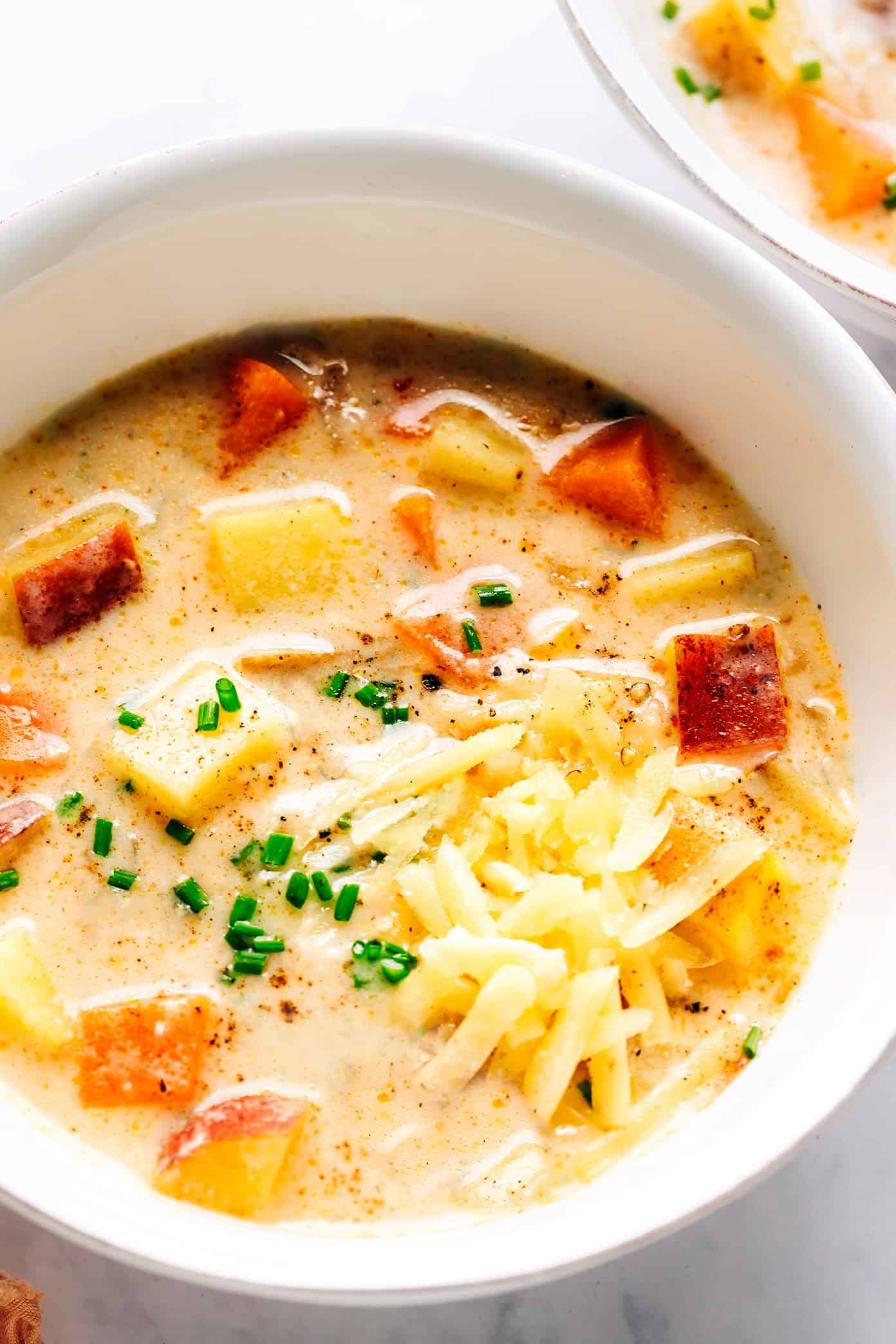 This Three Potato Soup is made with a zesty, creamy cheddar broth and a sweet and savory combination of Yukon gold potatoes, red potatoes, and sweet potatoes. Easy to make in about 30 minutes and always so delicious and comforting! Feel free to leave the soup vegetarian, or add in some bacon, ham, sausage or chicken if you prefer. (Gluten-free and vegan options included too.) | gimmesomeoven.com Bowl of three potato soup with cheddar and chives