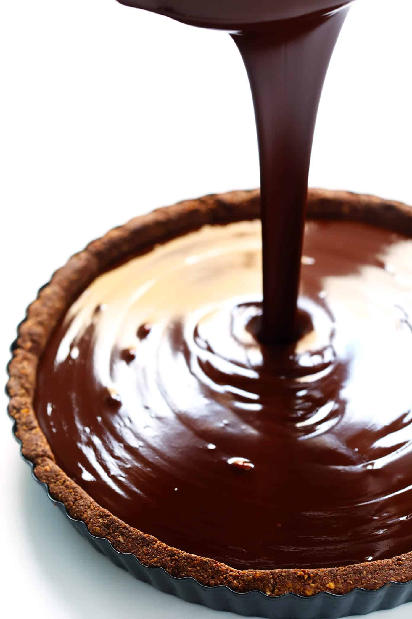 LOVE this Salted Dark Chocolate Tart recipe! It's quick and easy to make ahead, made with a gluten-free almond crust and zero heavy cream, and it's SO decadent and delicious. The perfect dessert for Valentine's Day or anytime you're craving some chocolate. | Gimme Some Oven #chocolate #tart #darkchocolate #dessert #sweets #valentines #glutenfree #vegan #vegetarian Pouring dark chocolate filling into tart pan