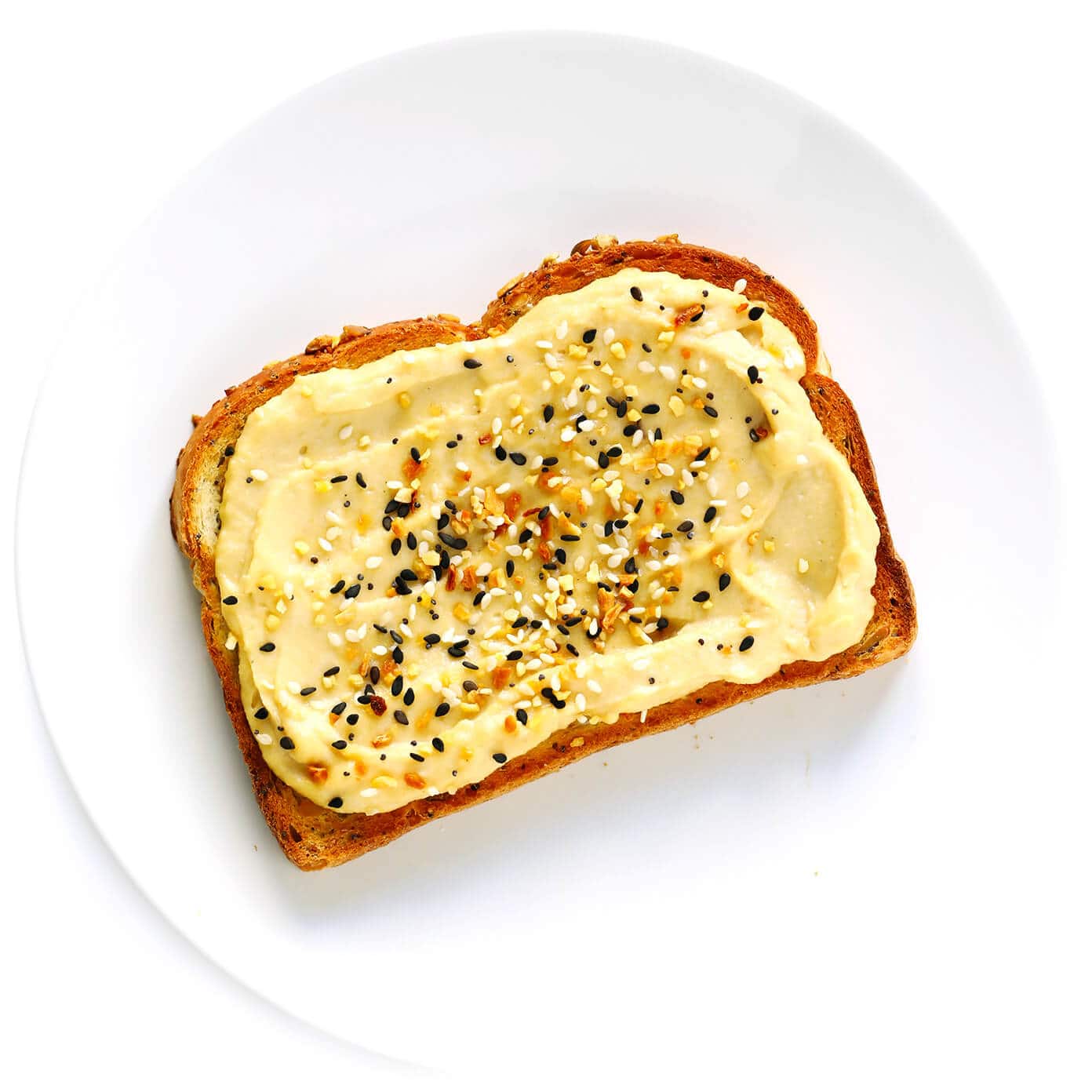 Hummus Toast is fun to customize with your favorite toppings, and makes for a delicious easy breakfast, lunch, dinner or healthy snack! Read more for details on 8 of our favorite toppings -- "everything", avocado, elote, tomato basil, lox, fried egg, mediterranean or honey banana. | gimmesomeoven.com #hummus #toast #healthy #breakfast #dinner #lunch #snack "Everything" Bagel Seasoning on Hummus Toast