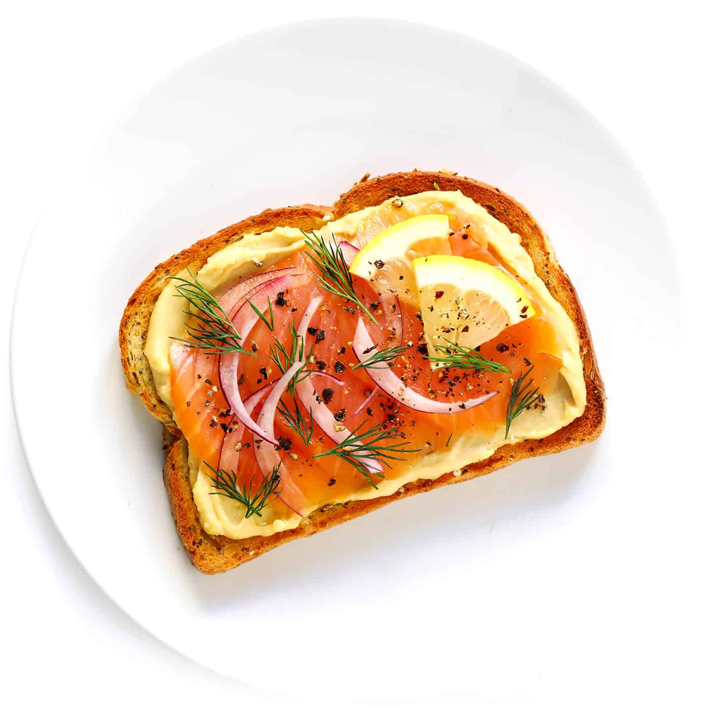 Hummus Toast is fun to customize with your favorite toppings, and makes for a delicious easy breakfast, lunch, dinner or healthy snack! Read more for details on 8 of our favorite toppings -- "everything", avocado, elote, tomato basil, lox, fried egg, mediterranean or honey banana. | gimmesomeoven.com #hummus #toast #healthy #breakfast #dinner #lunch #snack Smoked Salmon (Lox) Hummus Toast