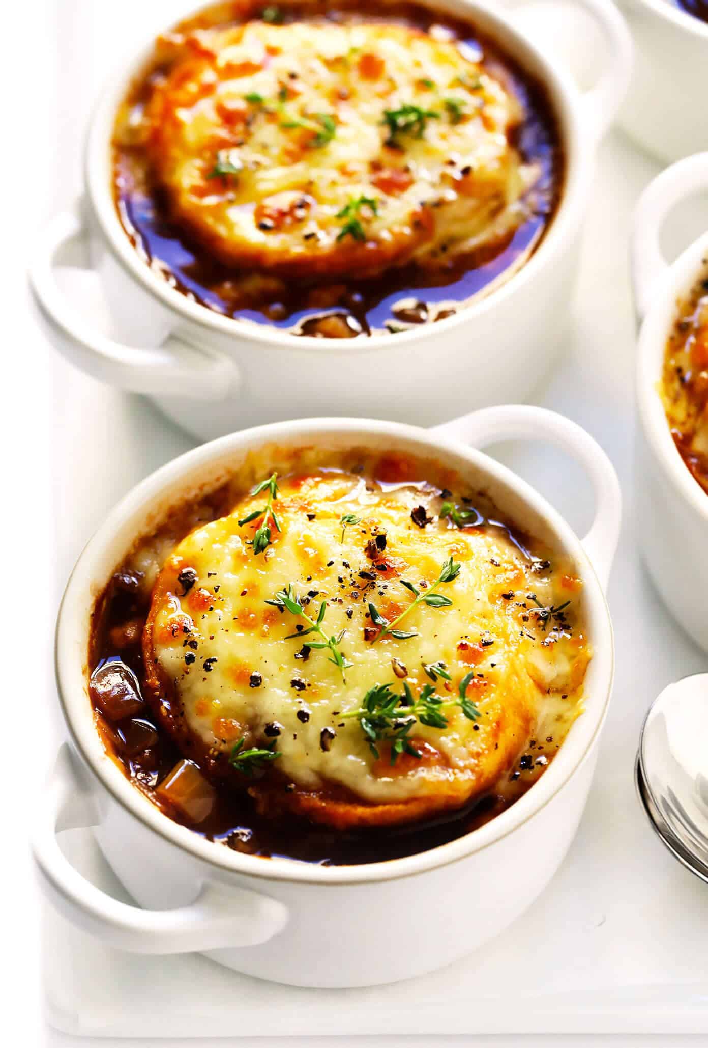 The BEST French Onion Soup recipe! It's easy to make, full of delicious caramelized onions, and topped with the classic cheesy baguette slices. A delicious vegetarian dinner recipe, perfect for fall and winter. | gimmesomeoven.com #onion #soup #dinner #vegetarian #recipe #caramelized #french #mealprep French Onion Soup in Bowls with Melted Cheese and Thyme