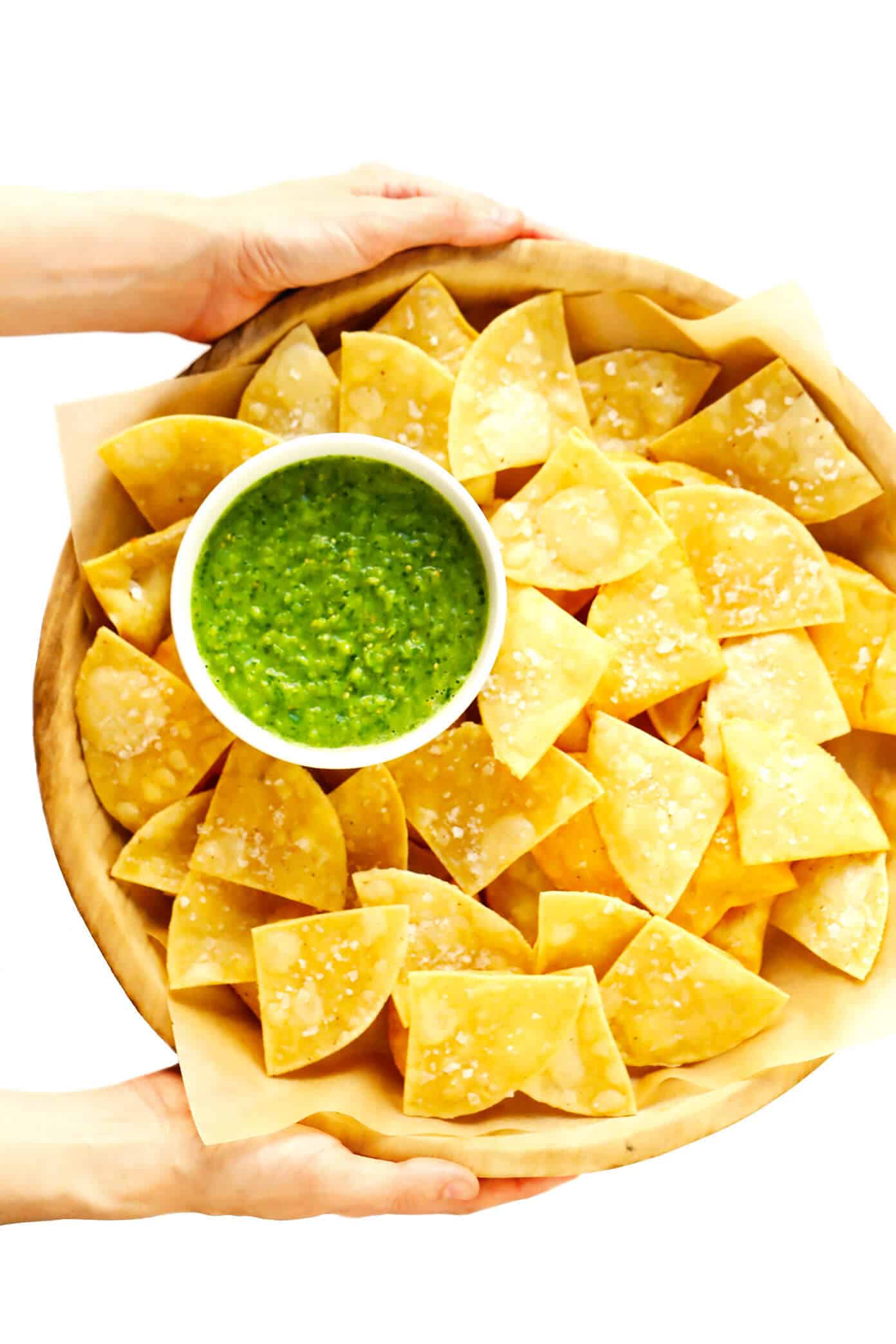 This fresh ("cruda") salsa verde recipe is easy to make in 5 minutes with raw tomatillos and avocado, and tastes refreshingly sweet, light and delicious! Serve with tortilla chips or fries, drizzle on burgers or kabobs, or whatever sounds good! | gimmesomeoven.com #salsa #verde #tomatillo #mexican #raw #glutenfree #vegan #vegetarian #healthy #sauce Holding a bowl of Fresh Salsa Verde with Homemade Chips