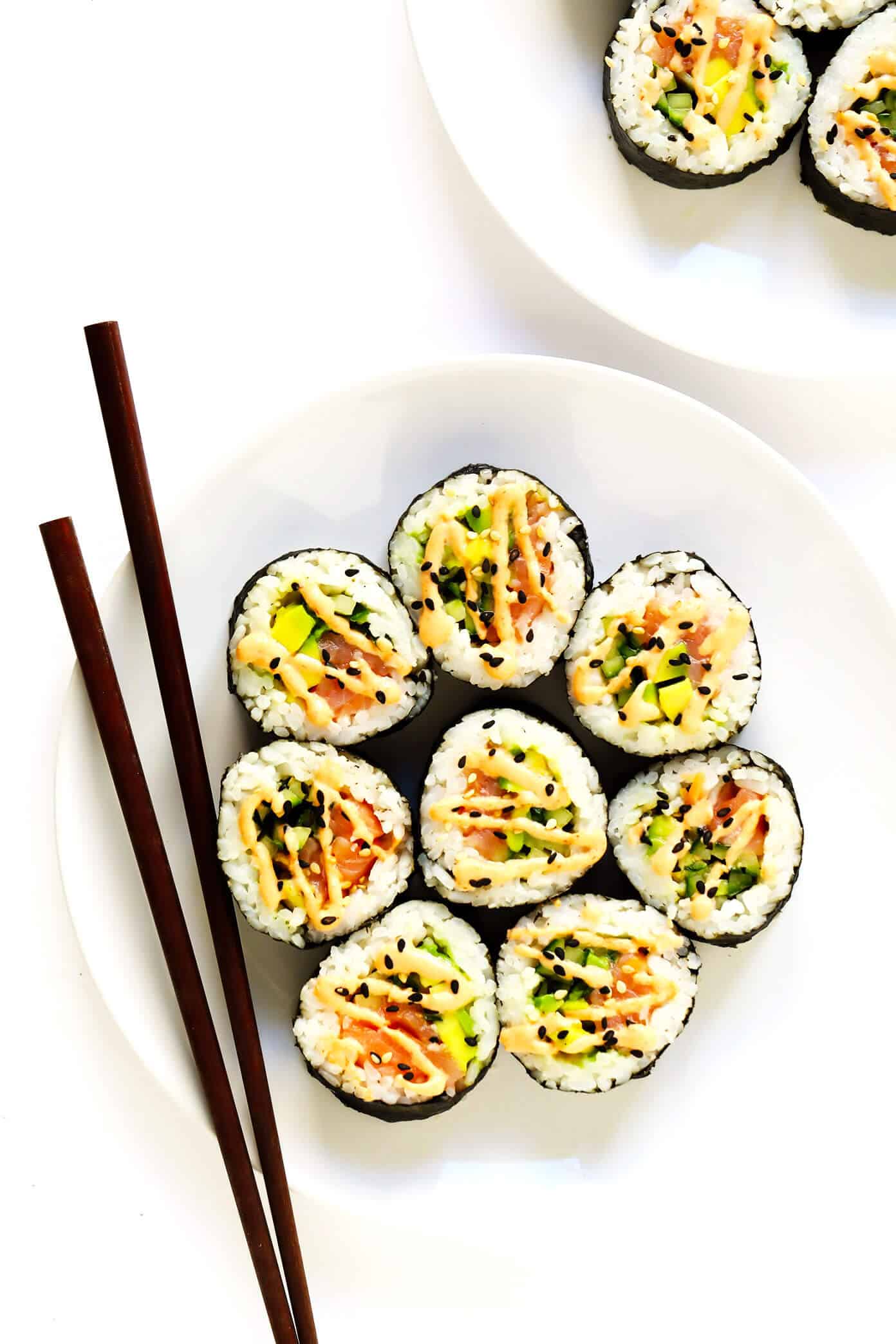 Learn how to make sushi rolls with this easy maki rolls recipe! They are surprisingly easy to make, and 100% customizable with whatever ingredients you love best. Spicy sriracha sauce recipe included if you would like to make spicy tuna, salmon or veggie rolls! | gimmesomeoven.com #sushi #rolls #maki #japanese #howto #salmon #vegetarian #vegan #healthy #dinner #entertaining Plates of Spicy Salmon Avocado Maki Rolls with Chopsticks