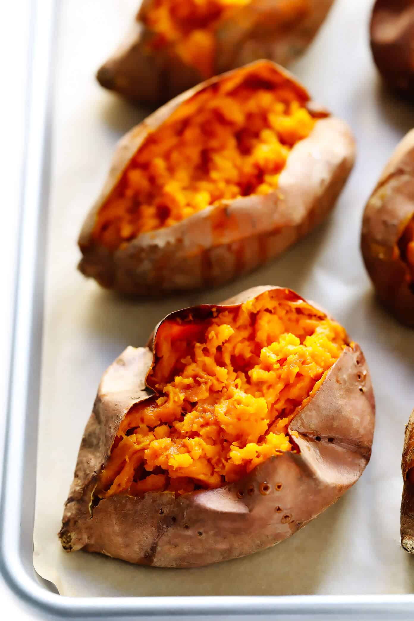 My favorite method for how to bake sweet potatoes in the oven that are perfectly crispy on the outside and soft on the inside. Plus, lots of ideas for loaded potato toppings you can add on too! | gimmesomeoven.com #sweetpotato #healthy #glutenfree #vegan #vegetarian #dinner #side Plain baked sweet potatoes on a baking sheet