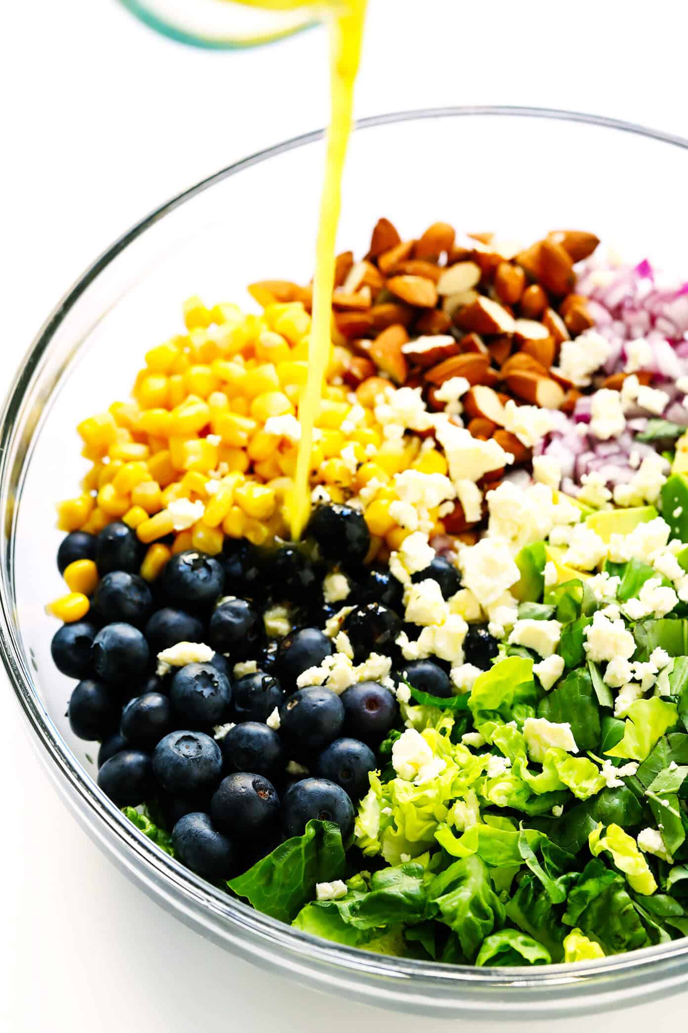 This Blueberry, Corn & Avocado Chopped Salad recipe is tossed with lots of fresh basil, toasted almonds, crumbled feta, red onions, and an easy lemon dressing. The perfect salad for summertime! | gimmesomeoven.com #salad #blueberry #corn #avocado #chopped #glutenfree #healthy #dinner #vegetarian #summer Drizzling lemon dressing into blueberry salad
