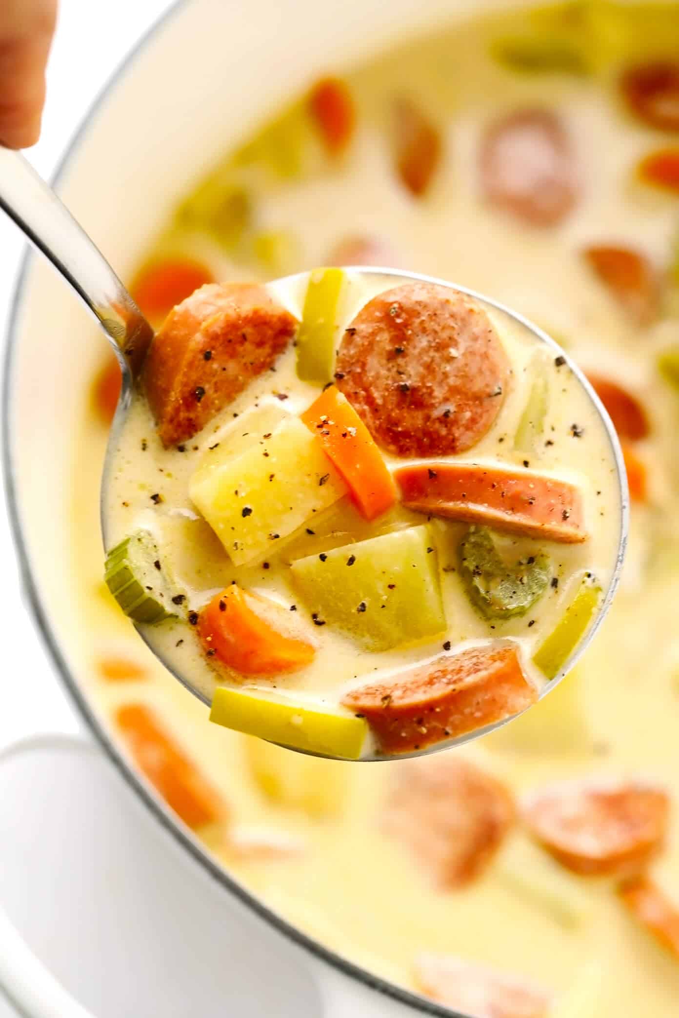 This Smoked Sausage, Apple and Potato Soup recipe is easy to make and simmered in the yummiest creamy broth made with coconut milk (or cream) and zesty Old Bay seasoning. The perfect easy dinner recipe to warm you up on a chilly night! | gimmesomeoven.com Smoked Sausage, Apple and Potato Soup Closeup in Ladle
