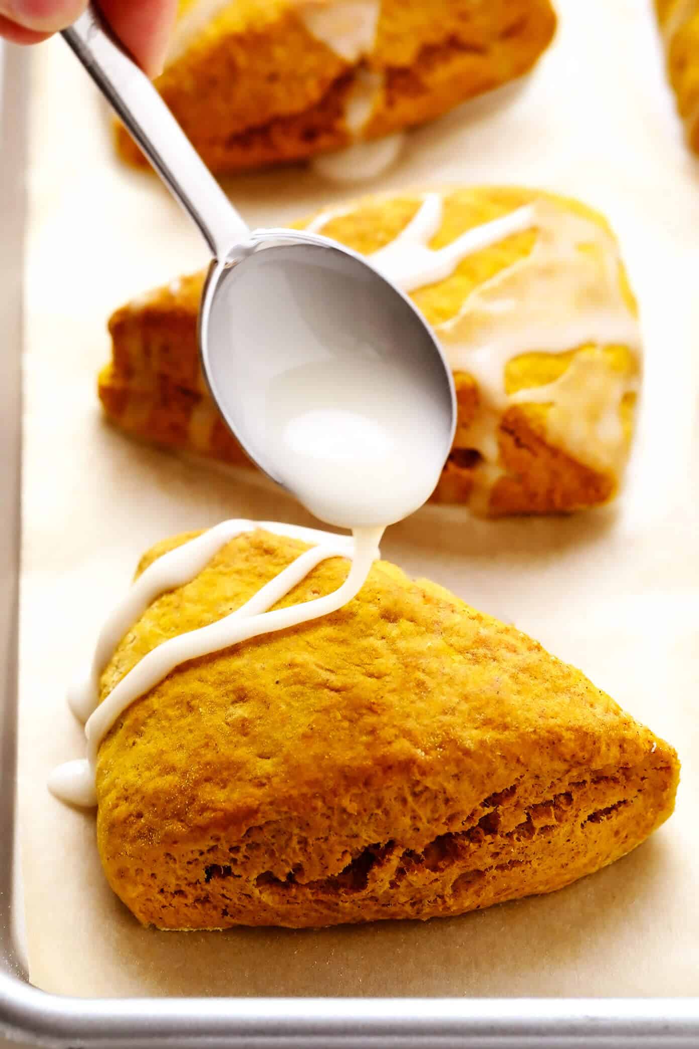 This pumpkin scones recipe is quick and easy to make, drizzled with a light vanilla glaze, and full of the best cozy pumpkin flavors. The perfect fall treat for breakfast, brunch, snack or dessert. | gimmesomeoven.com #pumpkin #scone #breakfast #brunch #dessert #treat #vanilla #glaze #icing #easy Drizzling Vanilla Glaze on Pumpkin Scones