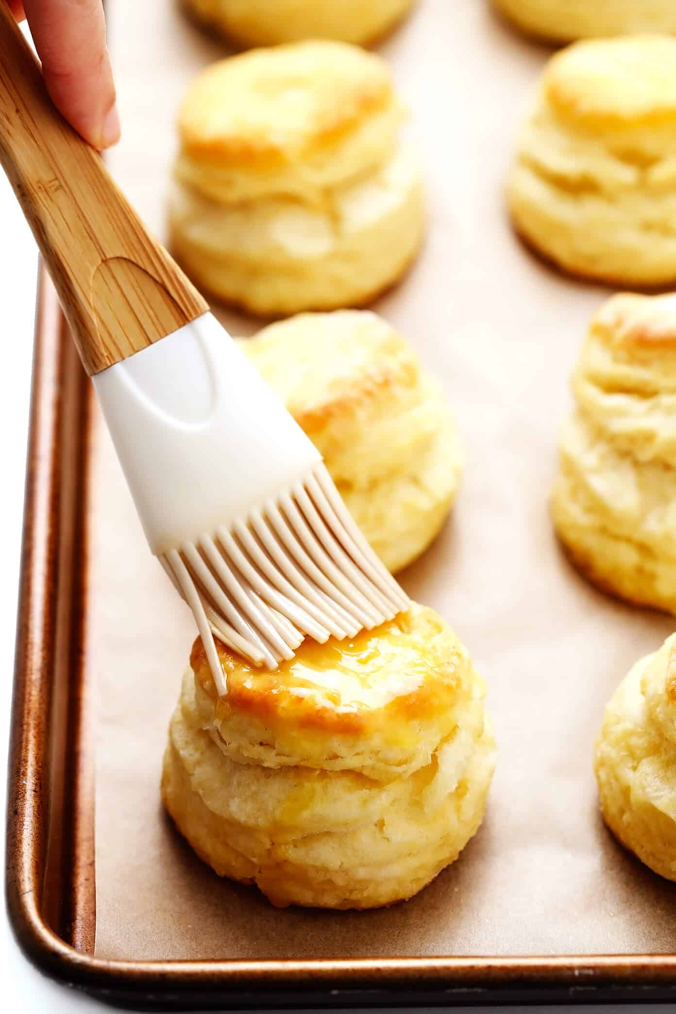 My favorite homemade buttermilk biscuit recipe -- easy to make, perfectly soft and tall and flaky, and always SO buttery and delicious. Serve them for breakfast with jam or gravy, as a side dish for lunch or dinner, or as a topping for chicken pot pie or your favorite casserole! | gimmesomeoven.com #biscuit #roll #bread #recipe #buttermilk #breakfast #brunch #side #vegetarian #baking Brushing butter on homemade biscuits