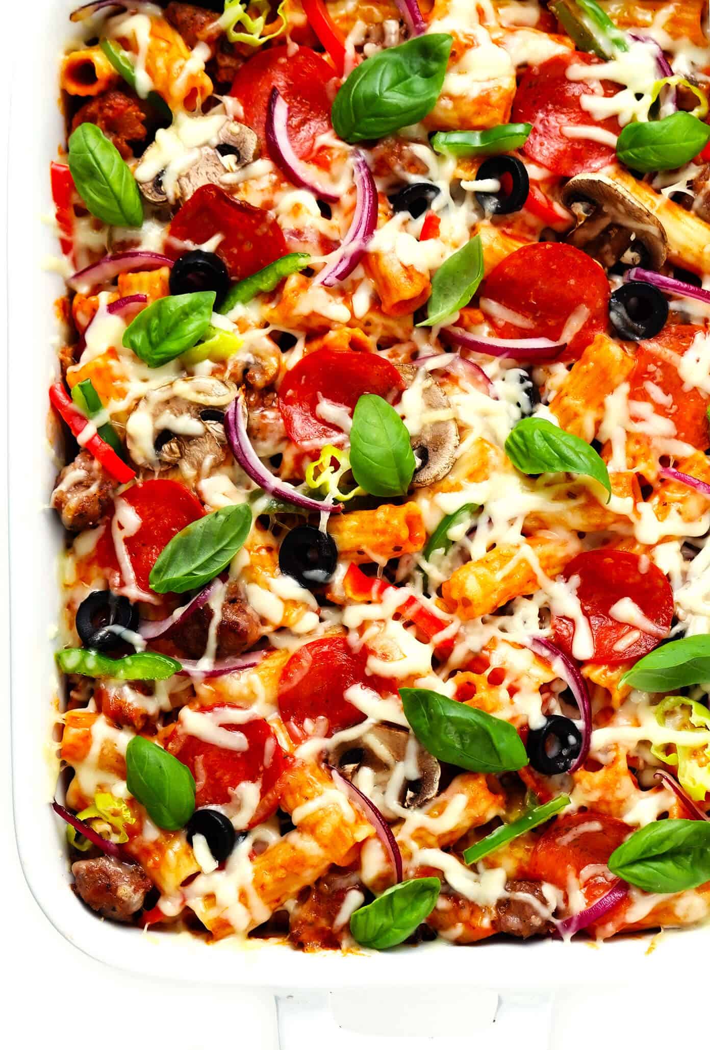 This "Pizza" Baked Ziti recipe is totally fun to make with all of your favorite pizza toppings! Simply bake them up with your favorite pasta, marinara sauce and cheeses, then serve up this casserole while it's hot and bubbly for a delicious Italian dinner! Feel free to use gluten-free, vegetarian and/or vegan ingredients if you prefer. | gimmesomeoven.com #pizza #pasta #bakedziti #casserole #bake #italian #dinner #easy #vegetarian #glutenfree Pizza Baked Ziti in Baking Dish with Basil Garnish