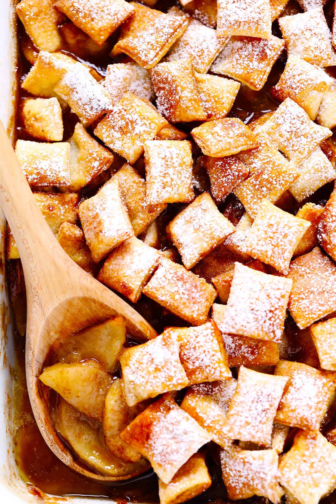This easy Apple Pandowdy recipe is made with a delicious baked apple cinnamon pie filling topped with toasted puff pastry bites and a light dusting of powdered sugar. Absolutely delicious served warm with vanilla ice cream, and the perfect dessert for the holidays. | gimmesomeoven.com #apple #pandowdy #pie #dessert #bake #crisp #puffpastry #filling #thanksgiving #christmas Apple Pandowdy In Pan with Wooden Spoon