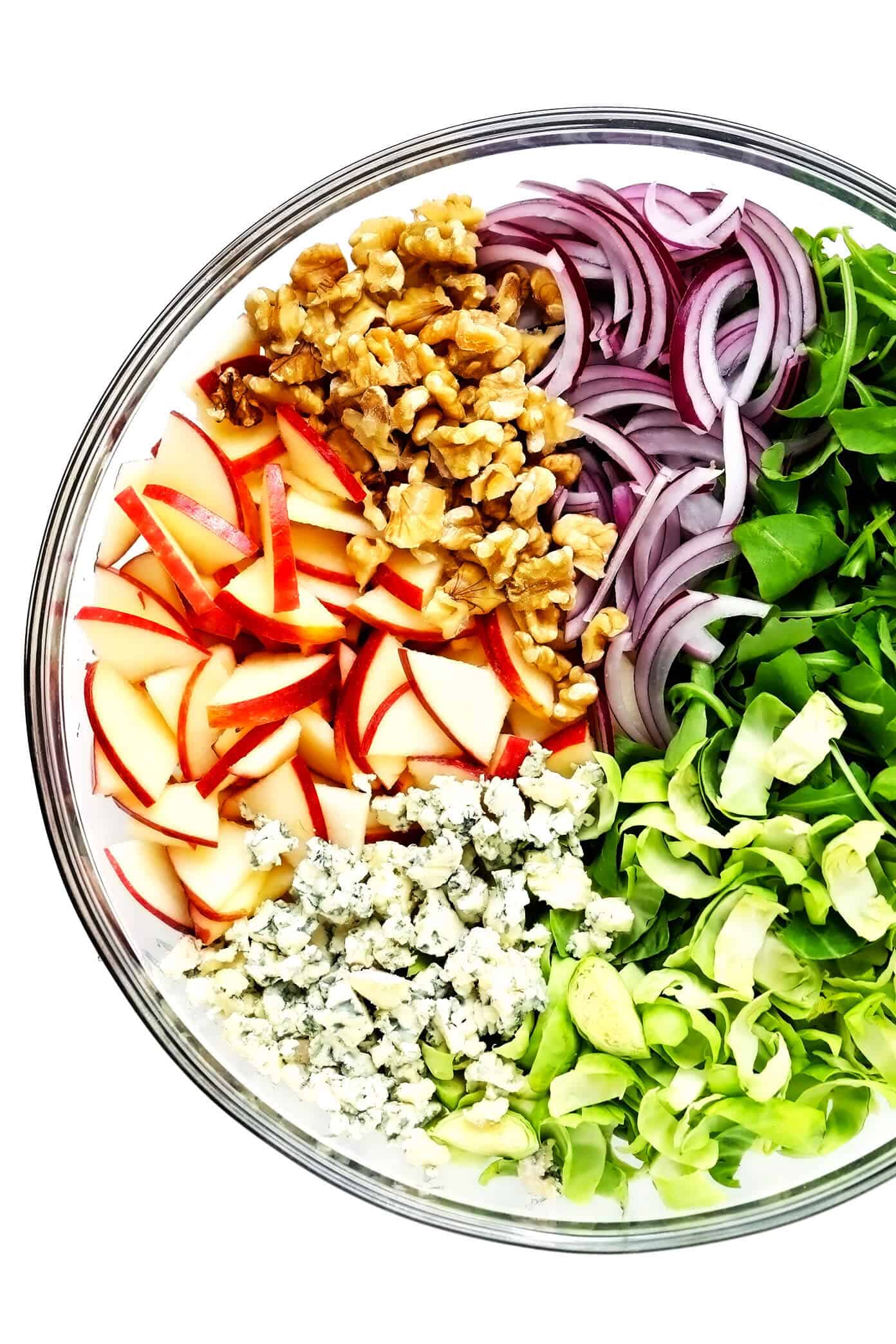 This shredded Brussels Sprouts Salad recipe is tossed with chopped arugula, sweet apples, crisp red onions, toasted nuts (walnuts, pecans, or almonds), crumbled soft cheese (blue, goat or feta), and my simple everyday salad dressing. Perfect for the holidays or winter weeknights! | gimmesomeoven.com #brussels #apple #salad #healthy #thanksgiving #christmas #holiday #glutenfree #vegetarian #dinner #side Bowl with Apples, Walnuts, Red Onion, Arugula, Shredded Brussels and Blue Cheese