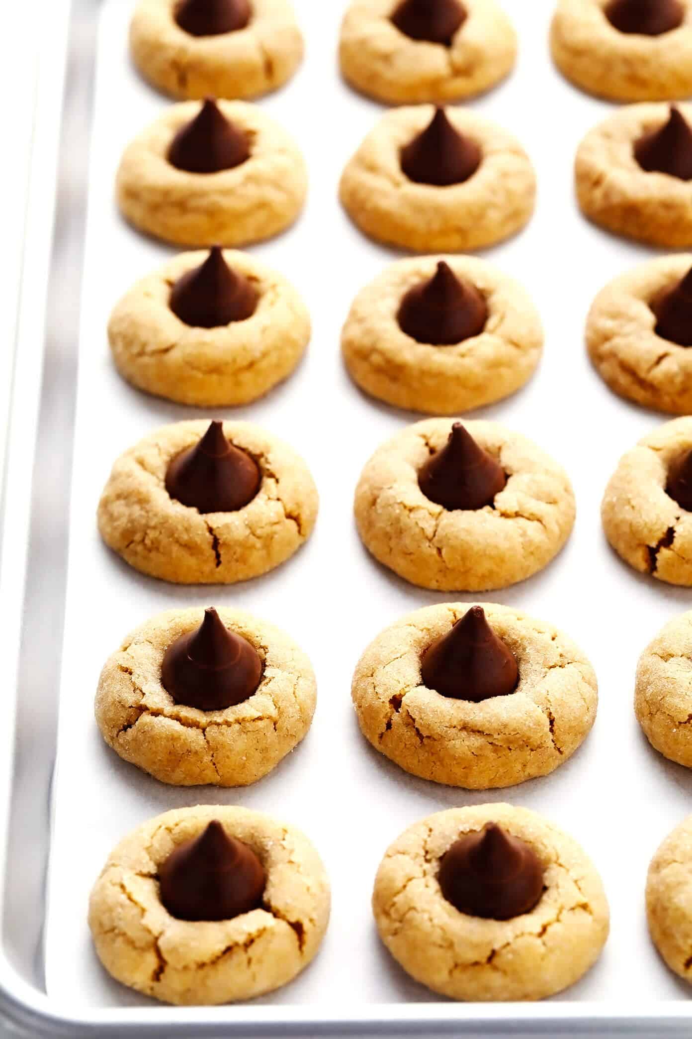 This peanut butter blossoms recipe is made with extra peanut butter, topped with Hershey's Kisses (or peanut butter cups), and perfectly soft and chewy and crackled. Perfect for Christmas or holiday baking, or anytime you have a cookie craving! | gimmesomeoven.com Peanut Butter Blossoms on Cookie Sheet