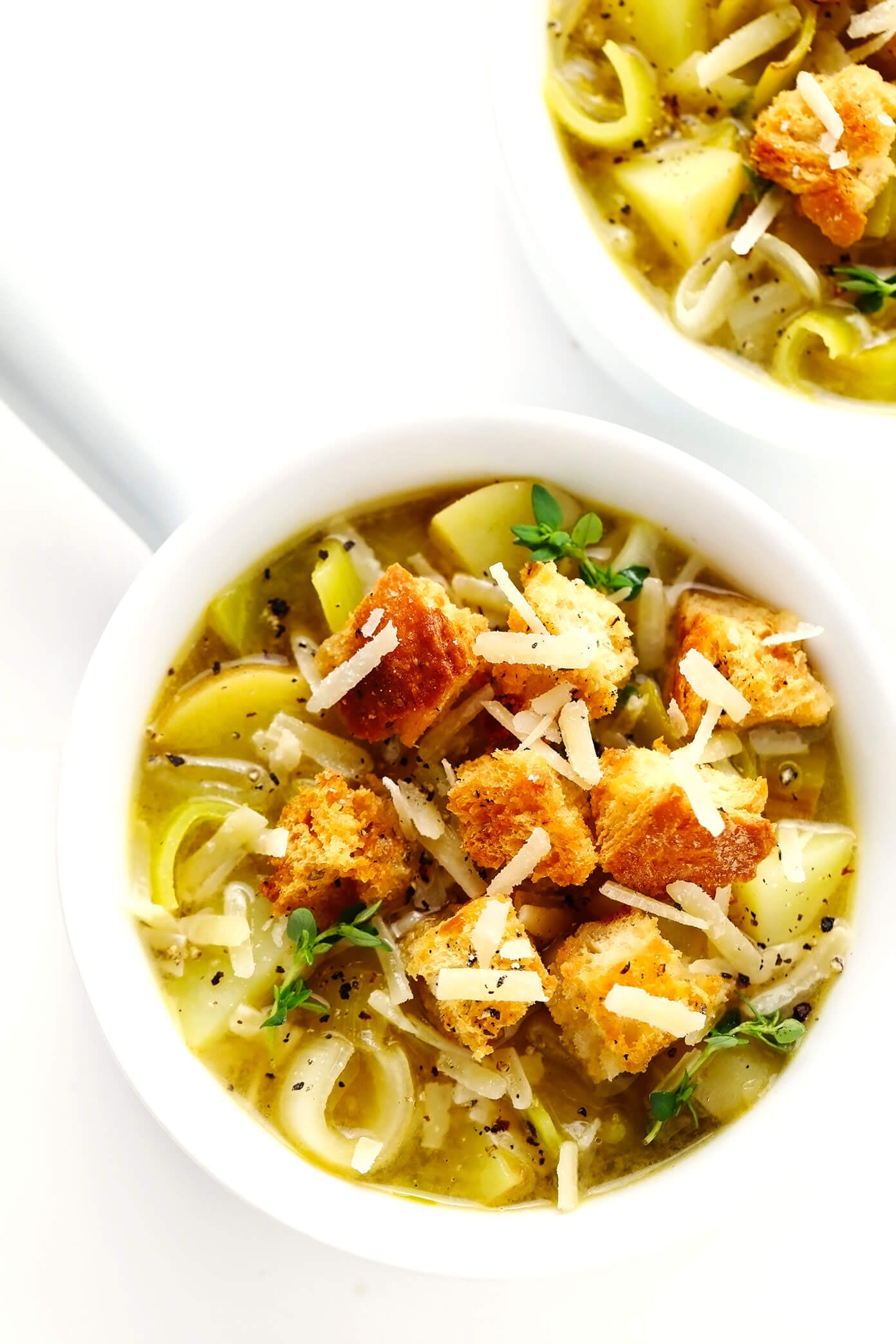 This Rustic Potato Leek Soup is easy to make in about 35 minutes, it's naturally gluten-free, vegetarian, vegan, and it's made with the most delicious, light, garlic-herb broth. A quick, easy and healthy dinner recipe that's always so comforting! (Feel free to add croutons or a sprinkle of Parmesan cheese too!) | gimmesomeoven.com #soup #potato #leek #french #onion #healthy #glutenfree #vegetarian #vegan #dinner #mealprep Bowls of Rustic Potato Leek Soup with Homemade Croutons and Parmesan