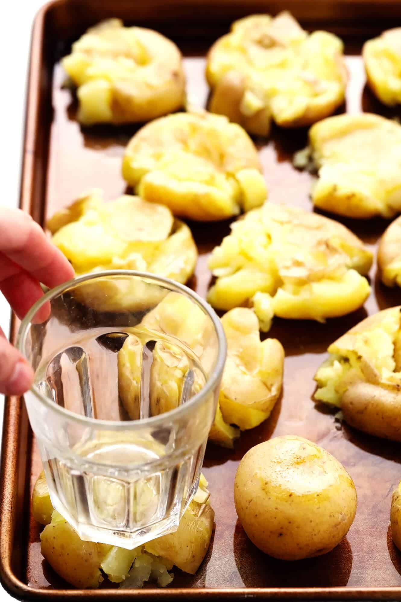 This Smashed Potatoes recipe is easy to make, irresistibly soft and crispy, and full of the best garlicky, buttery flavors. Feel free to add cheese, fresh herbs, or a pinch of flaky sea salt to this simple side dish if you'd like too! | gimmesomeoven.com #smashed #potatoes #roasted #garlic #butter #side #christmas #holiday #dinner Smashing boiled potatoes with a drinking glass
