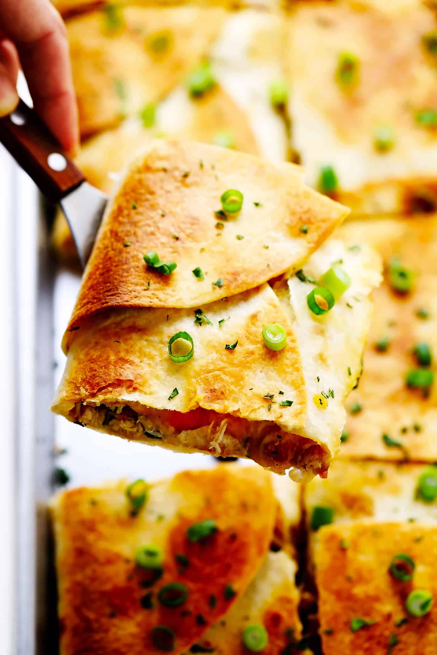 This party-sized chicken sheet pan quesadilla recipe is filled with a zesty mix of cheese, beans, veggies and baked up in a large sheet pan to feed a crowd. Serve as an appetizer, dinner entrée or game day snack with guacamole, salsa, sour cream or any of your favorite dips and enjoy! | gimmesomeoven.com #chicken #quesadilla #mexican #gameday #dinner #party #appetizer #cheese Sheet Pan Quesadilla Slice