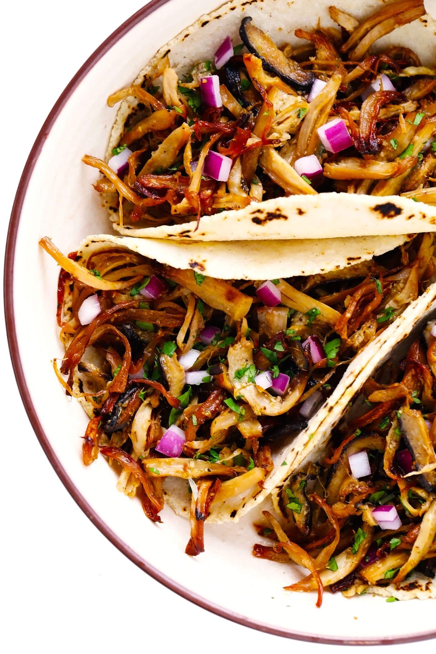 This Mexican mushroom "carnitas" recipe is fun and easy make with marinated shredded mushrooms that are roasted to crispy, juicy, delicious perfection! Vegetarian, vegan, gluten-free, and perfect for tacos, burritos, quesadillas and more. | gimmesomeoven.com #mushroom #carnitas #roasted #vegetarian #vegan #glutenfree #healthy #dinner #tacos Plate of Mushroom "Carnitas" Tacos with Red Onion and Cilantro