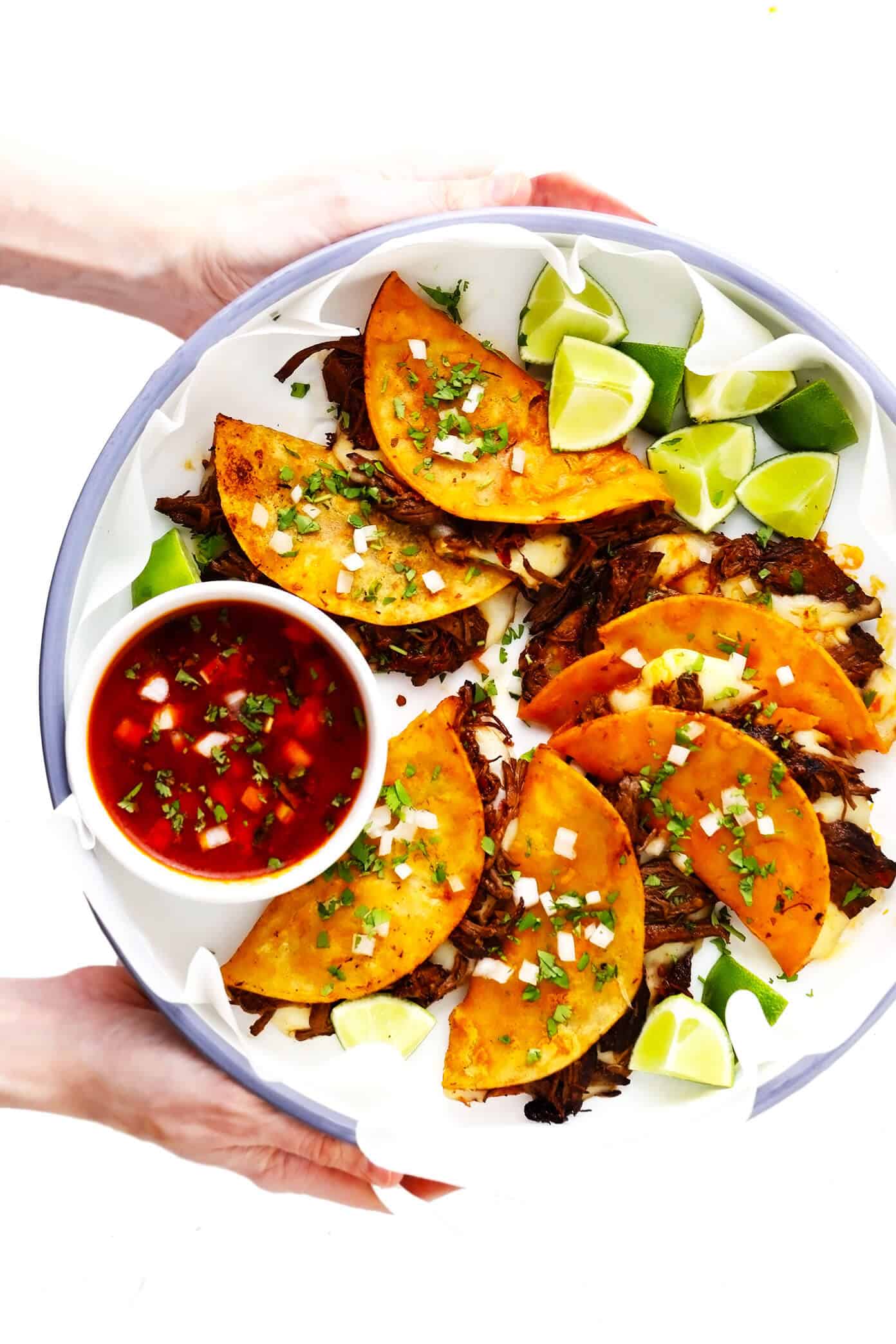 This birria tacos recipe (a.k.a. birria quesatacos) is made with tender birria beef, which is loaded into broth-dipped corn tortillas with cheese, fried until crispy, then dunked in birria broth for an extra-flavorful finish. Easy to make in either the Instant Pot, Crock-Pot or on the stovetop, and always a delicious Mexican dinner recipe! | gimmesomeoven.com #beef #birria #tacos #quesatacos #cheese #dip #sauce #fried #tortillas #jalisco #mexican Birria Quesatacos with Limes and Dipping Sauce