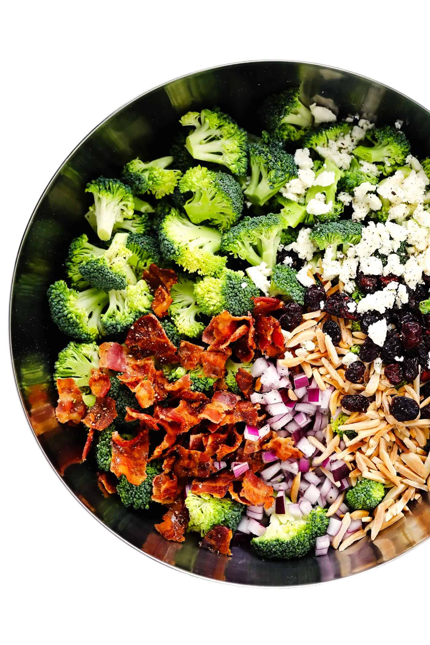 This classic broccoli salad recipe is made with fresh broccoli florets, crispy bacon, dried cranberries, toasted almonds, red onion, feta cheese, and a lightened-up creamy dressing. It's the perfect make-ahead side dish for picnics and potlucks and is always a crowd fave! | gimmesomeoven.com Broccoli Salad Ingredients In Bowl - Broccoli Florets, Bacon, Red Onion, Toasted Almonds, Dried Cranberries and Feta Cheese