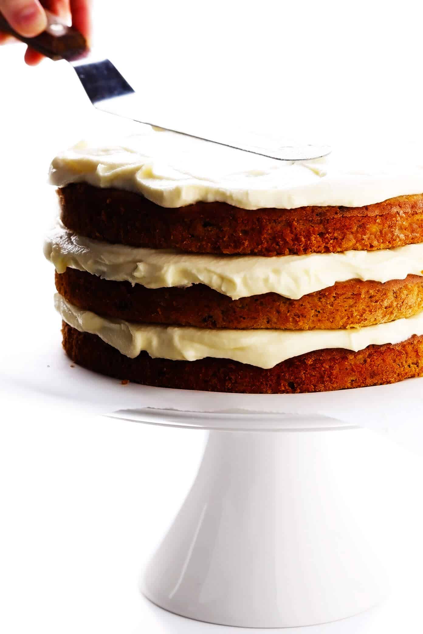 This delicious hummingbird cake recipe features ultra-moist pineapple banana cake layered with rich cream cheese frosting and a sprinkle of toasted pecans. It's the perfect dessert for spring, summer, or Easter and it's always a crowd fave! | gimmesomeoven.com #cake #dessert #hummingbird #jamaican #southern #creamcheese #frosting #icing #banana #pineapple #pecan Assembling hummingbird cake layers with cream cheese frosting