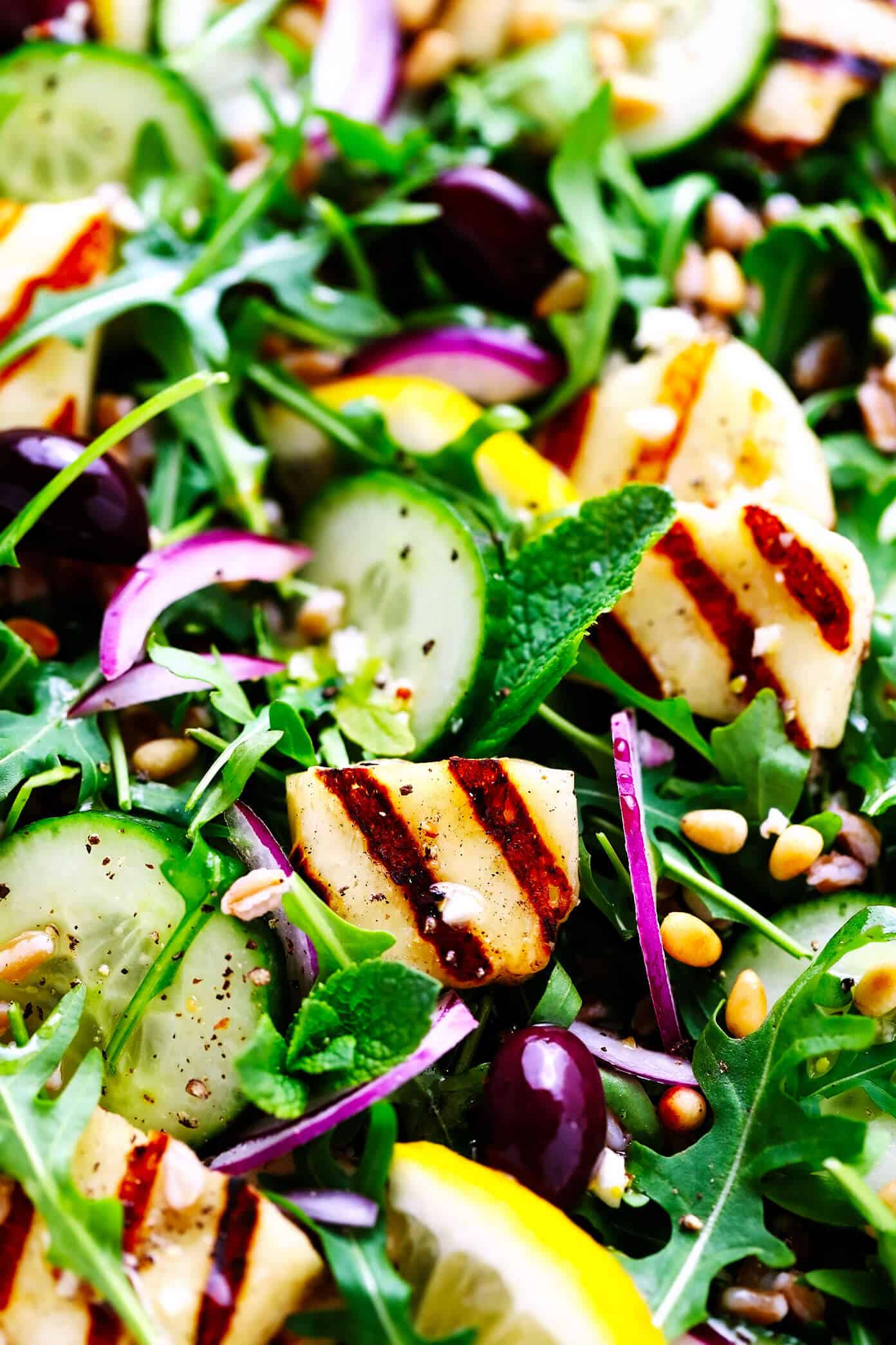 This Mediterranean-inspired grilled halloumi salad is easy to make with pan-grilled halloumi cheese, chewy farro, fresh cucumber and mint, and a zippy lemon dressing. It's the perfect side or entree salad to serve for dinner. And feel free to add in chicken, beef, shrimp or chickpeas if you'd like, too! | gimmesomeoven.com Grilled Halloumi Salad Closeup with Cucumber, Farro and Pine Nuts