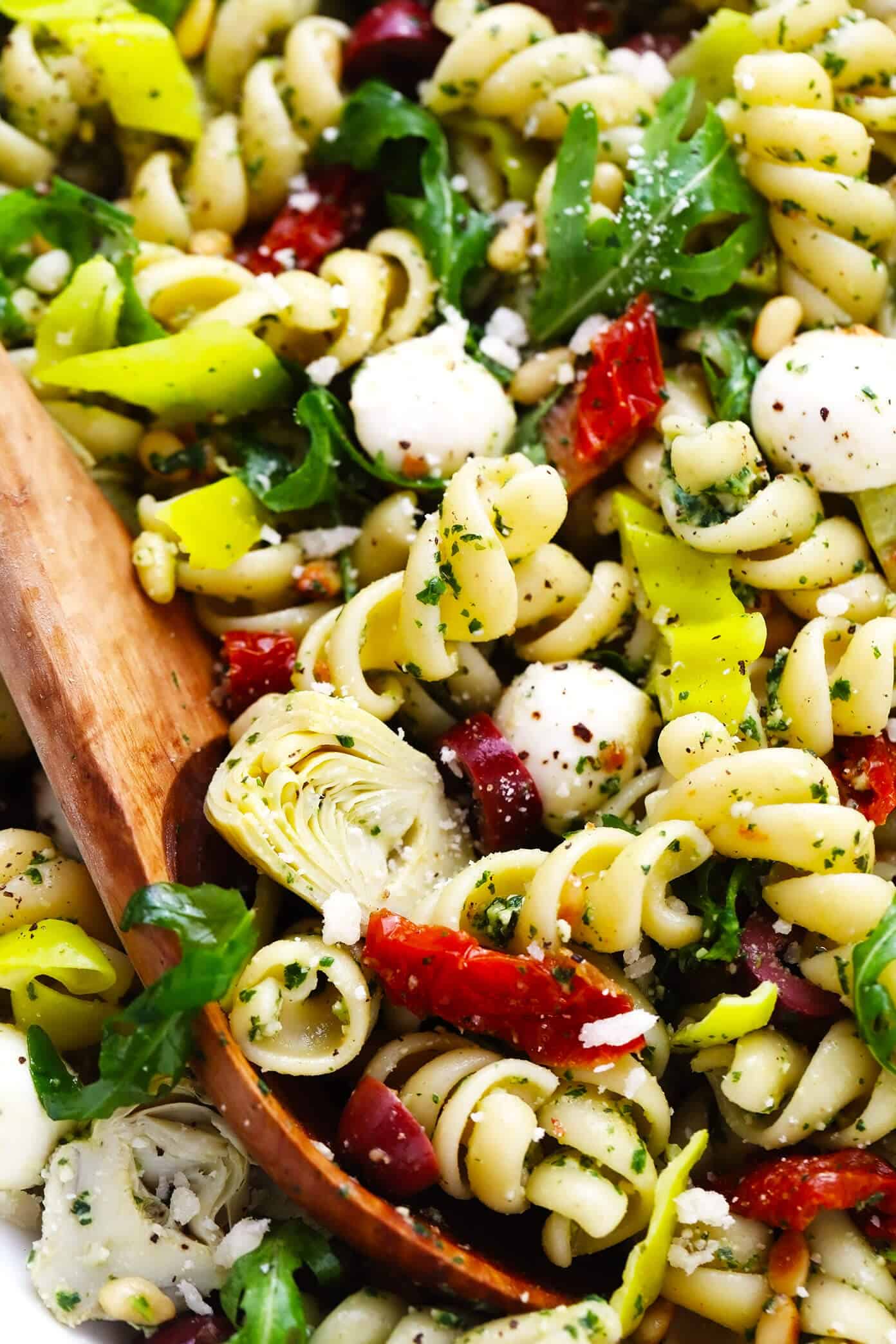 This Italian-inspired Pesto Pasta Salad recipe is loaded up with artichoke hearts, arugula, mozzarella, pepperoncini peppers, Kalamata olives, pine nuts and sprinkled with Parmesan. It's the perfect easy vegetarian side dish for summer grilling, parties and potlucks -- and easy to make gluten-free or vegan if you'd like too! | gimmesomeoven.com Italian Pesto Pasta Salad Closeup