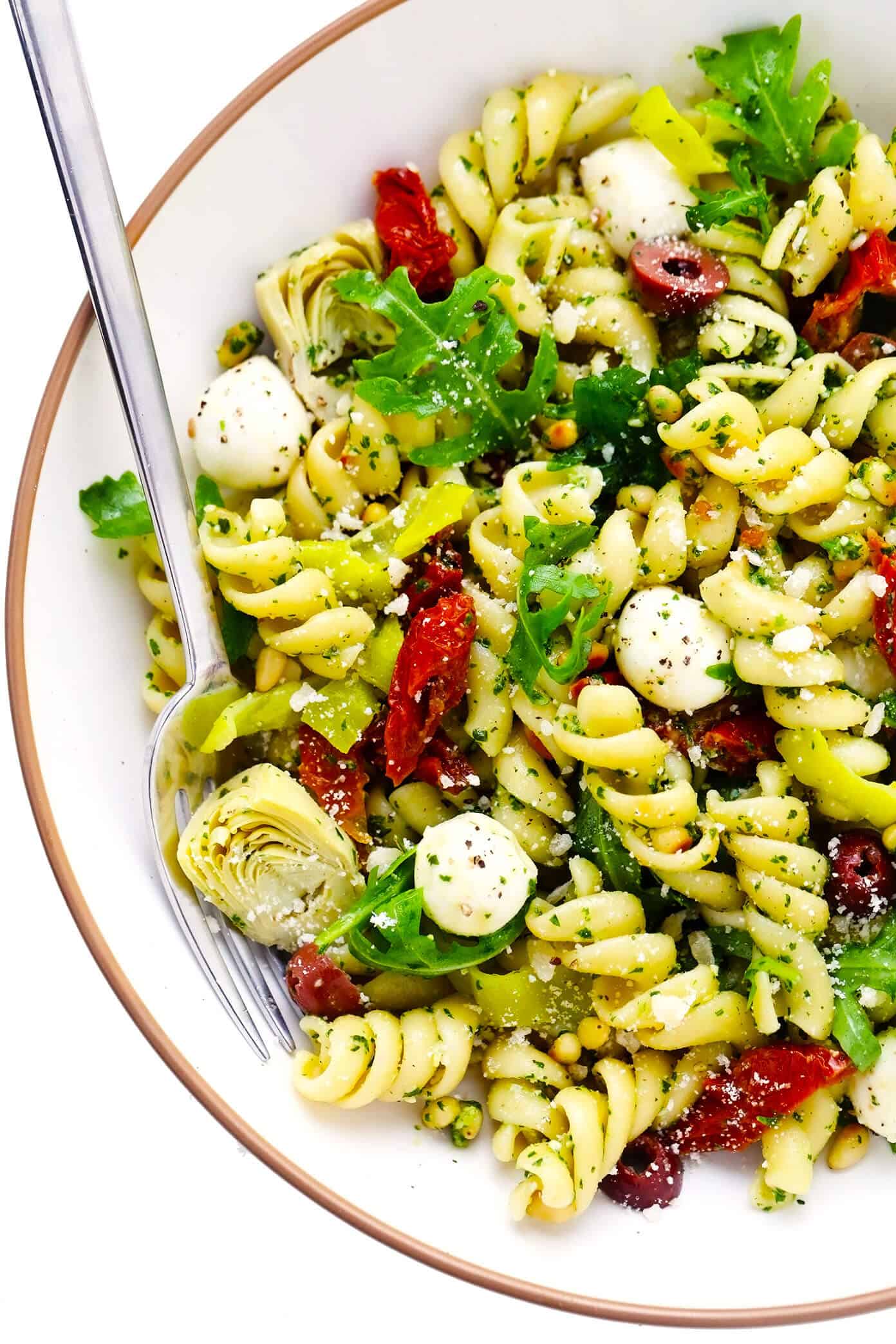 This Italian-inspired Pesto Pasta Salad recipe is loaded up with artichoke hearts, arugula, mozzarella, pepperoncini peppers, Kalamata olives, pine nuts and sprinkled with Parmesan. It's the perfect easy vegetarian side dish for summer grilling, parties and potlucks -- and easy to make gluten-free or vegan if you'd like too! | gimmesomeoven.com Pesto Pasta Salad in Bowl