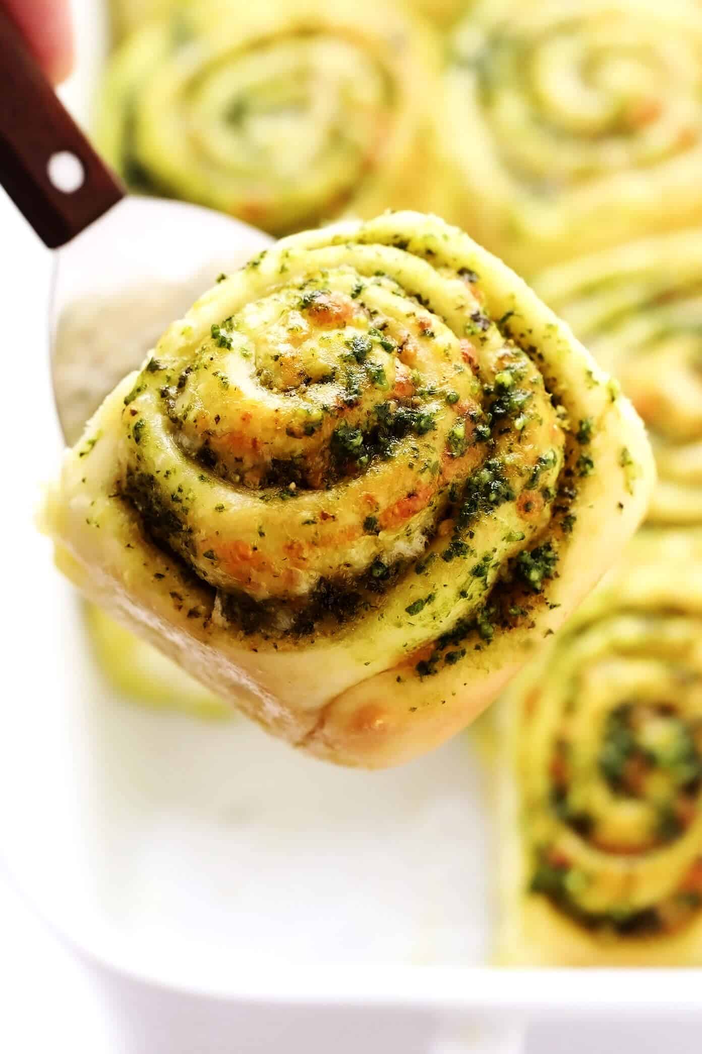 These deliciously cheesy pesto rolls are made with a buttery soft bread dough and swirled with fresh basil pesto, mozzarella and Parmesan cheese. Easy to make in about 1 hour and sure to be a favorite side dish! | gimmesomeoven.com Cheesy Pesto Roll Lifting Out of Pan