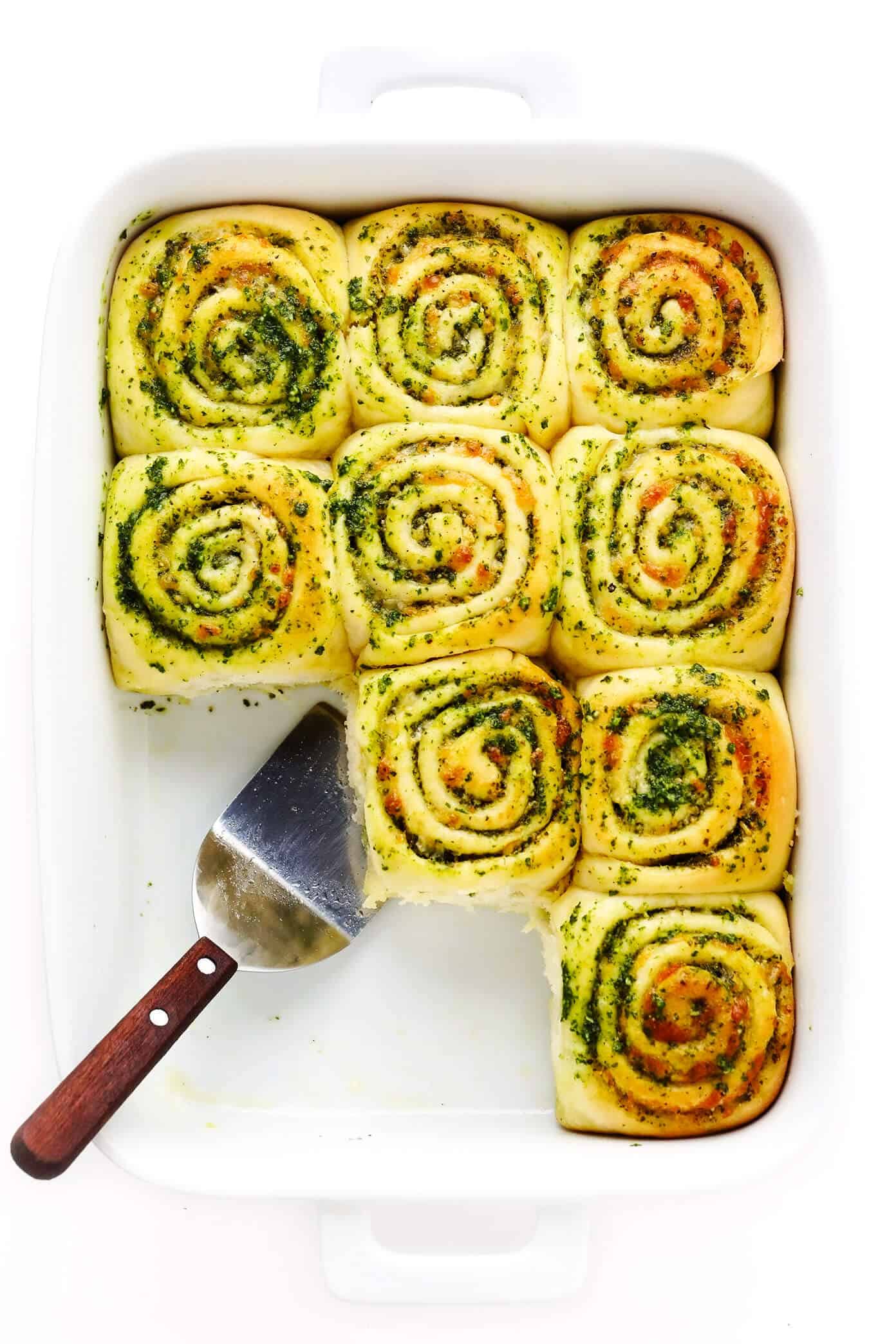 These deliciously cheesy pesto rolls are made with a buttery soft bread dough and swirled with fresh basil pesto, mozzarella and Parmesan cheese. Easy to make in about 1 hour and sure to be a favorite side dish! | gimmesomeoven.com Cheesy Pesto Rolls in Baking Dish