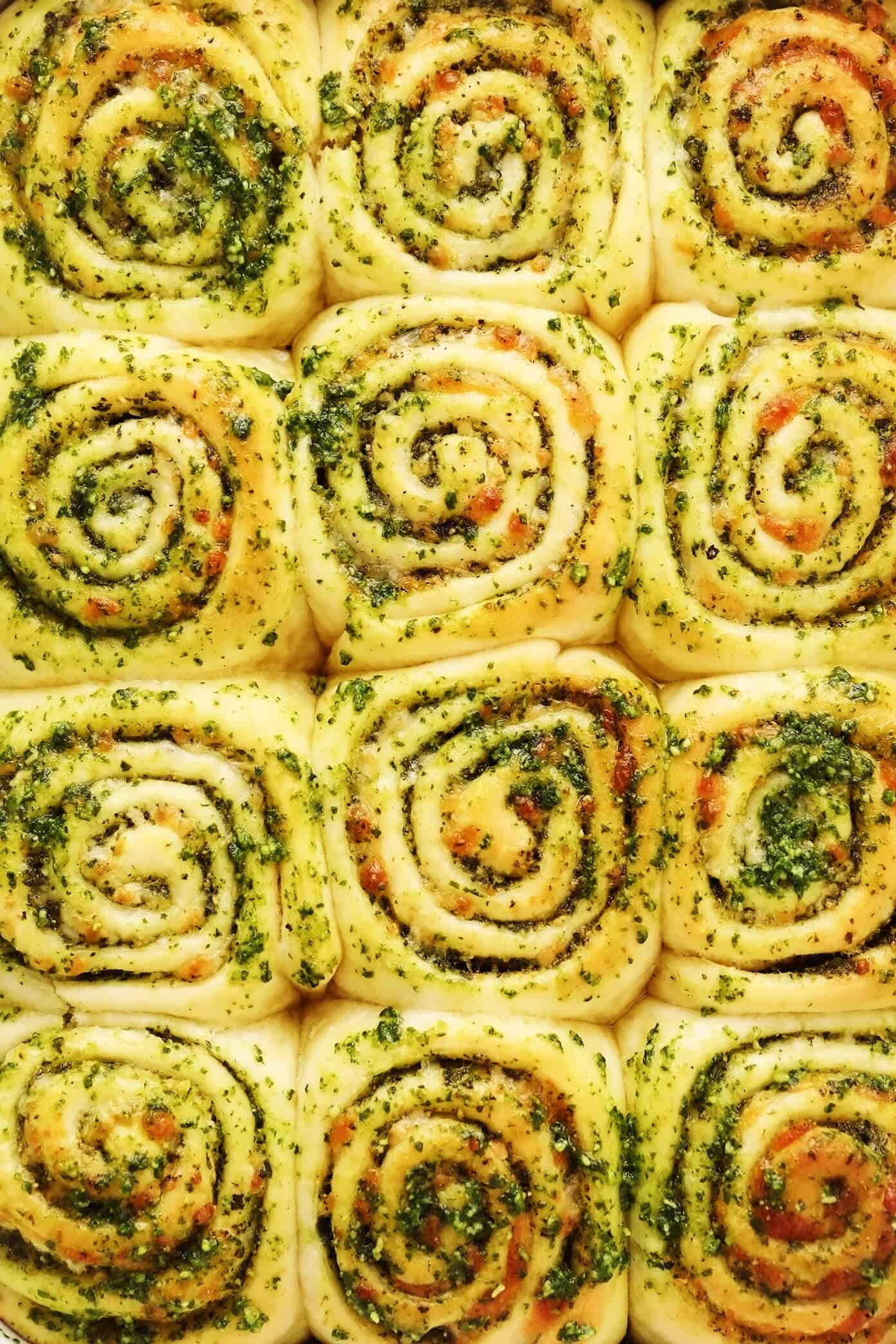 These deliciously cheesy pesto rolls are made with a buttery soft bread dough and swirled with fresh basil pesto, mozzarella and Parmesan cheese. Easy to make in about 1 hour and sure to be a favorite side dish! | gimmesomeoven.com Cheesy Pesto Swirl Rolls Closeup