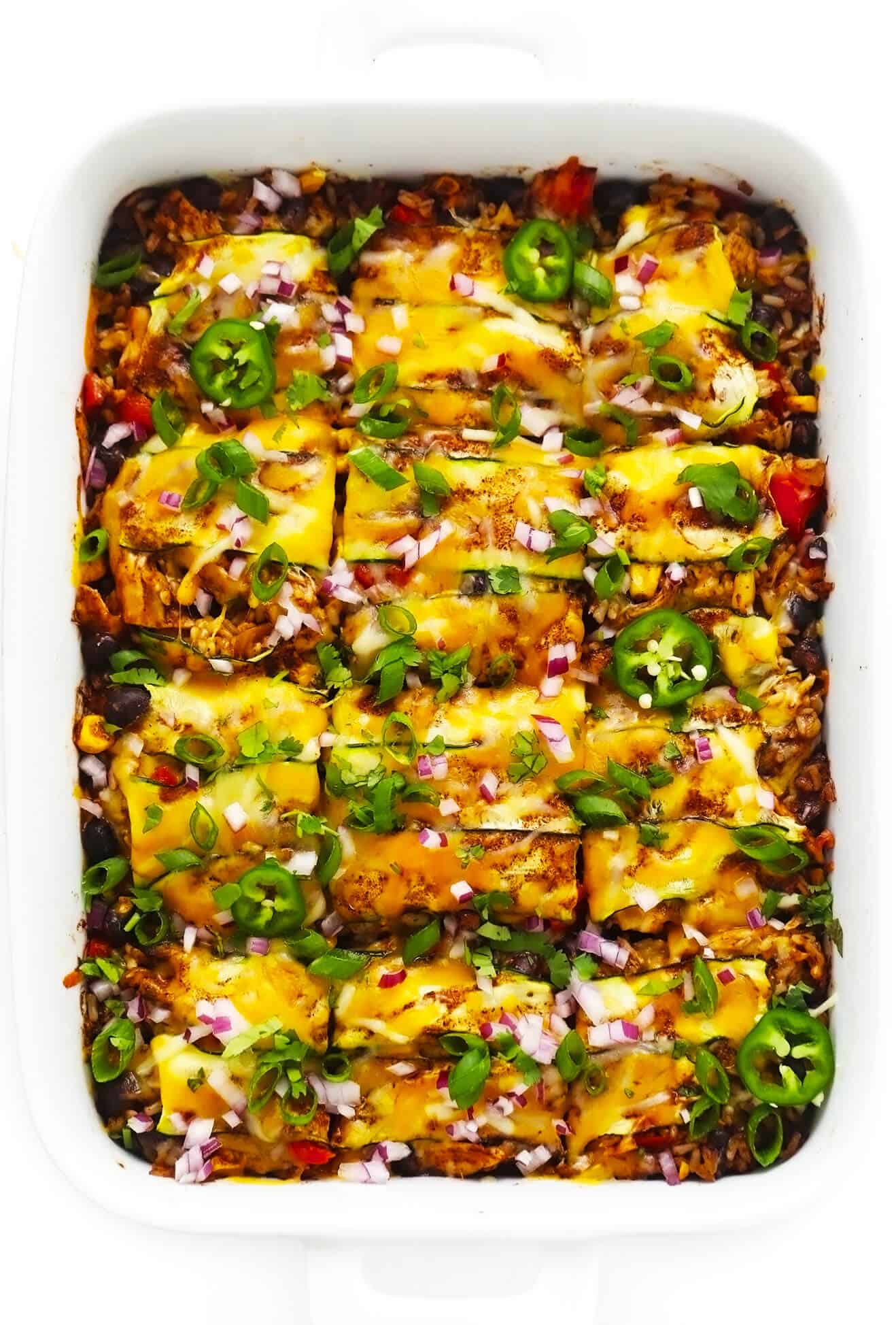 This Tex-Mex-inspired zucchini enchilada casserole is stacked (not rolled!) with layers of sliced zucchini, veggies, cheese, beans, rice and the most delicious homemade red enchilada sauce. It's naturally gluten-free and can be made with meat (chicken, beef, pork, chorizo, etc) or kept vegetarian. Serve it up for dinner with some avocado and enjoy! | gimmesomeoven.com Zucchini Chicken Enchilada Casserole in Baking Dish