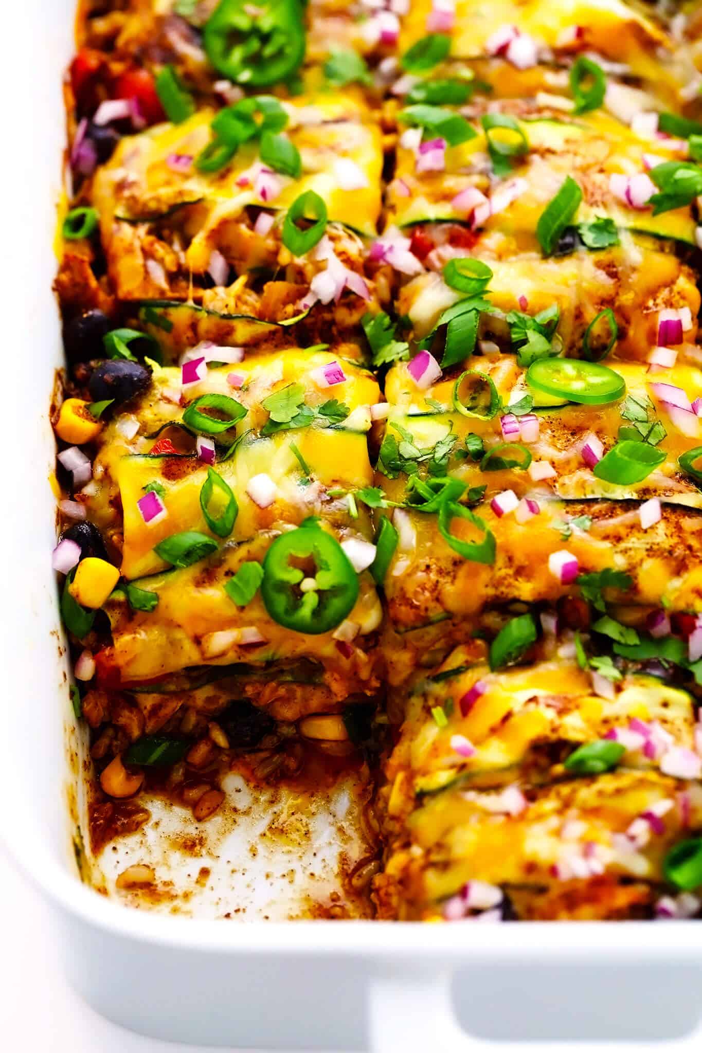 This Tex-Mex-inspired zucchini enchilada casserole is stacked (not rolled!) with layers of sliced zucchini, veggies, cheese, beans, rice and the most delicious homemade red enchilada sauce. It's naturally gluten-free and can be made with meat (chicken, beef, pork, chorizo, etc) or kept vegetarian. Serve it up for dinner with some avocado and enjoy! | gimmesomeoven.com Zucchini Chicken Enchilada Casserole in Baking Dish