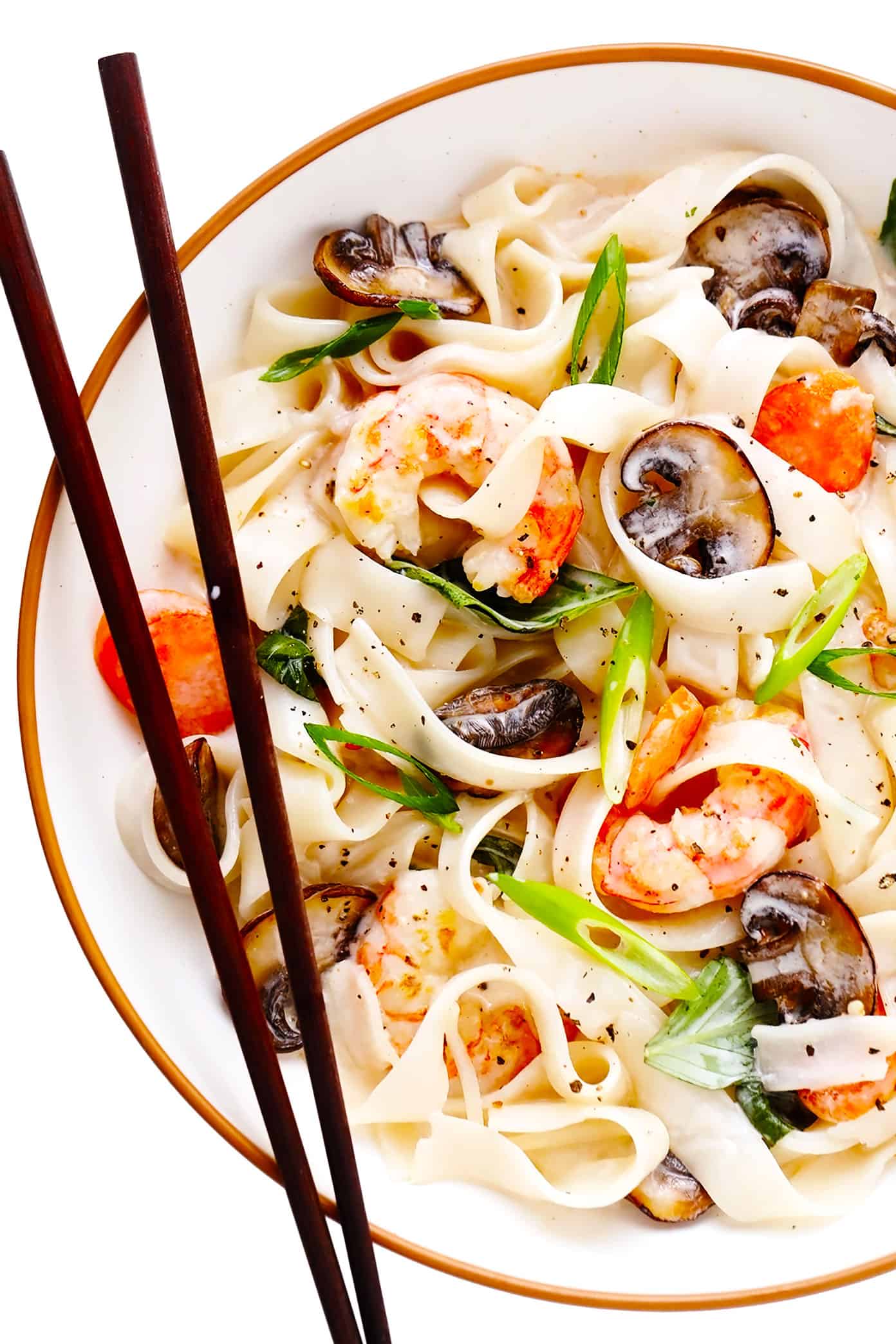 This Thai-inspired noodle stir-fry is tossed with fresh mushrooms and carrots, tender shrimp, and a zesty lemongrass ginger coconut sauce. Easy to make for dinner and full the best bright and citrusy flavors! Feel free to sub in chicken, beef, pork or tofu in place of the shrimp if you prefer. | gimmesomeoven.com Bowl of lemongrass coconut rice noodles with shrimp and chopsticks