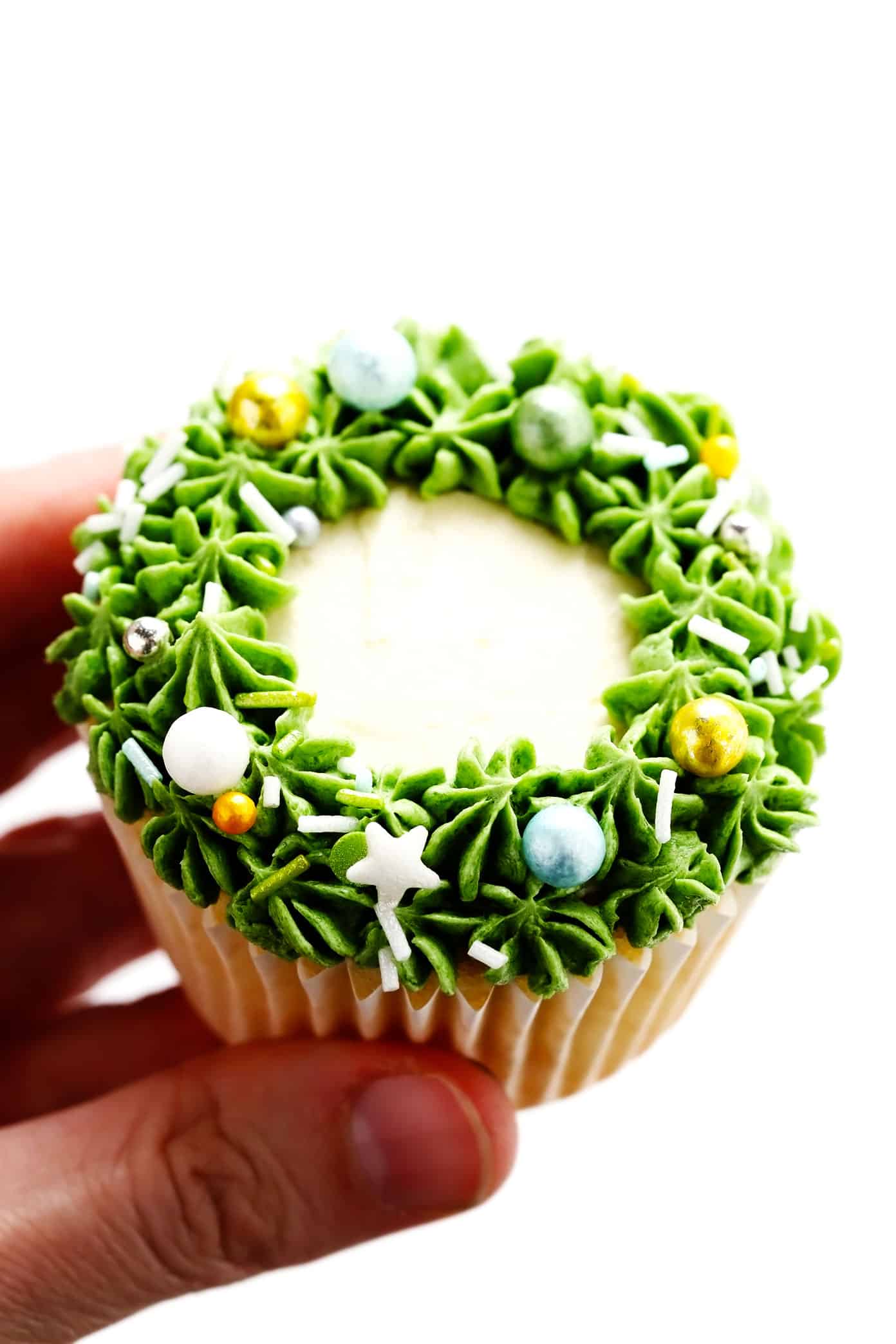 These cute Christmas cupcakes are made with soft and fluffy vanilla cupcakes, a simple vanilla buttercream frosting, and whatever fun sprinkles or toppings you choose. Decorating instructions and supply list included too for this fun holiday dessert! | gimmesomeoven.com Christmas Wreath Cupcake Closeup