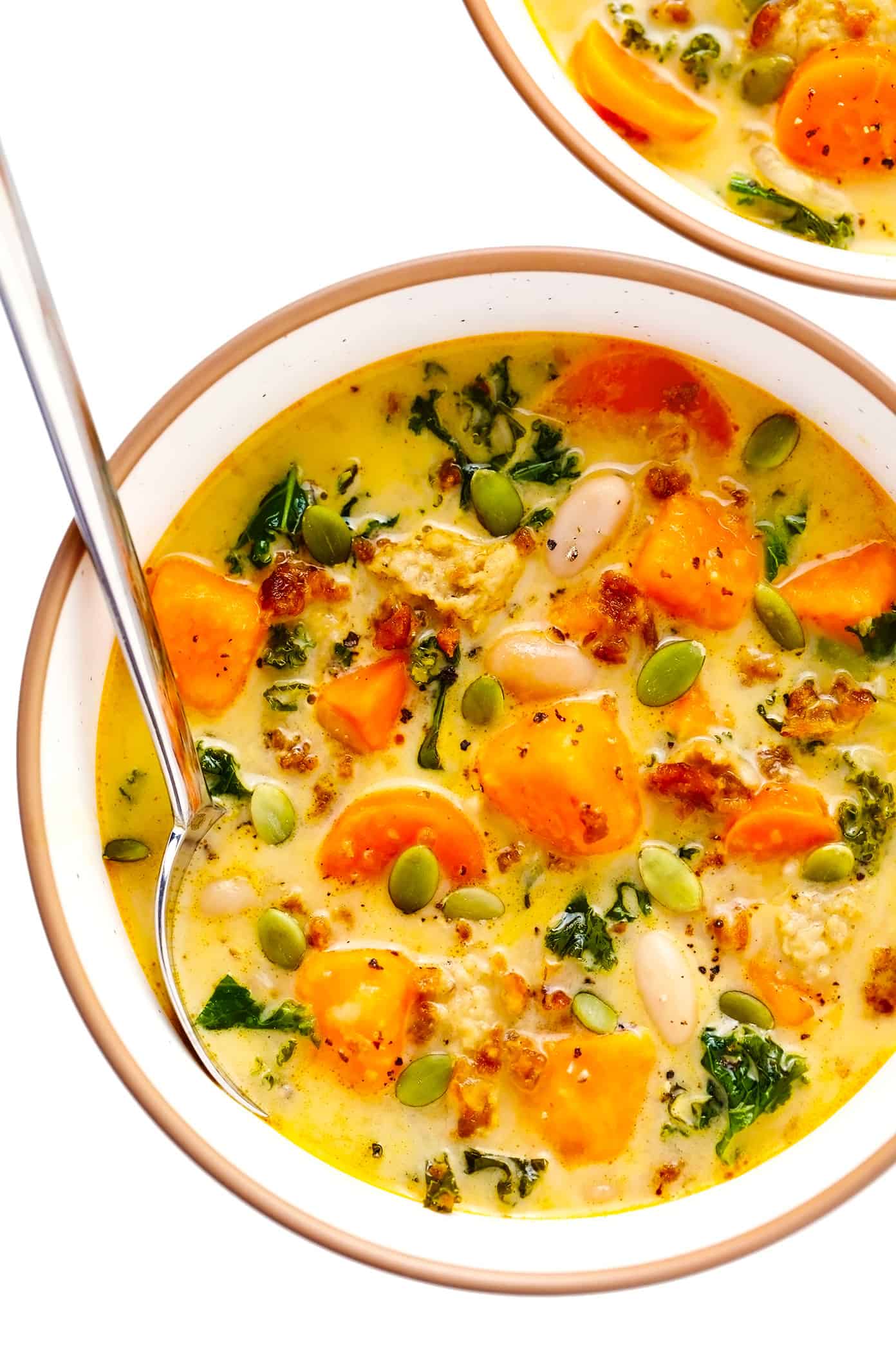 This Creamy Sweet Potato and Sausage Soup recipe is made with zesty sausage, seasonal veggies and kale, tender white beans, and a creamy, garlicky, paprika-sage broth. Easy to make vegan, if you use plant-based sausage, and naturally gluten-free. The perfect cozy dinner for fall and winter. | gimmesomeoven.com Serving bowl of creamy sweet potato and sausage soup with white beans and kale