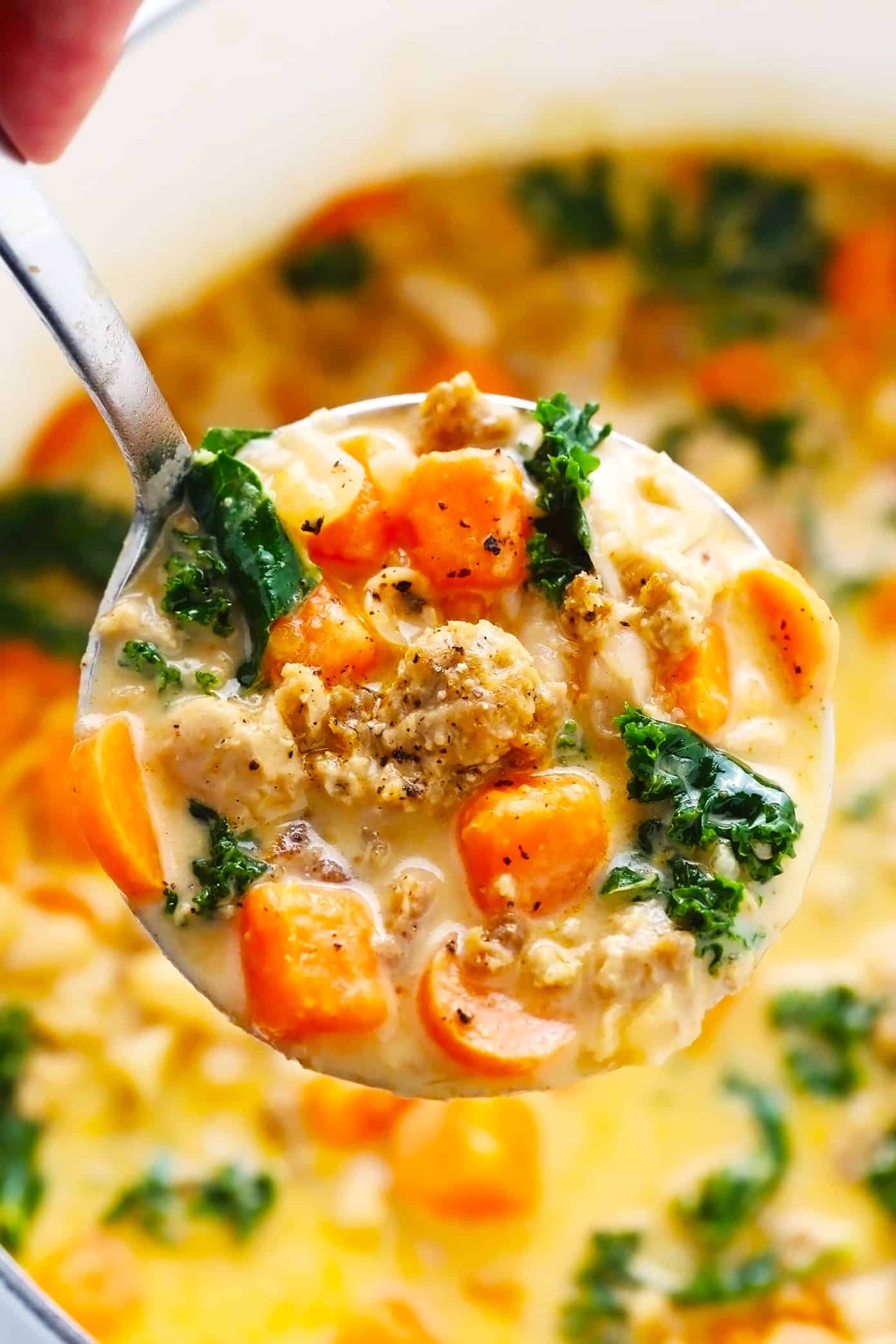 This Creamy Sweet Potato and Sausage Soup recipe is made with zesty sausage, seasonal veggies and kale, tender white beans, and a creamy, garlicky, paprika-sage broth. Easy to make vegan, if you use plant-based sausage, and naturally gluten-free. The perfect cozy dinner for fall and winter. | gimmesomeoven.com Ladle of Sweet Potato Soup